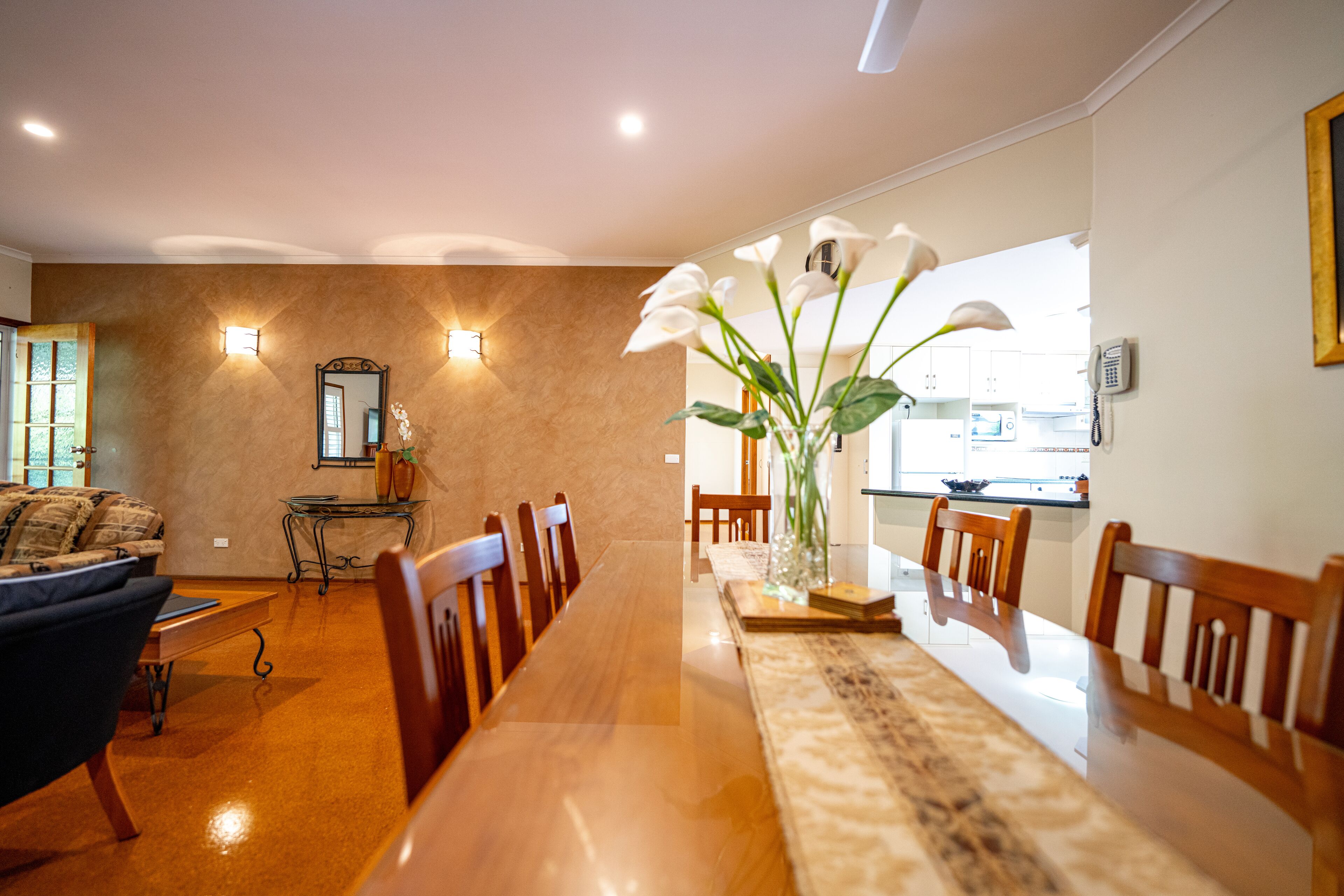 A dining area with a long wooden table, chairs, and a vase with flowers.