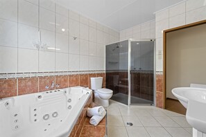 A modern bathroom with a bathtub, toilet, and glass-enclosed shower. - Birds 'n' Bloom Cottages (Yungaburra)