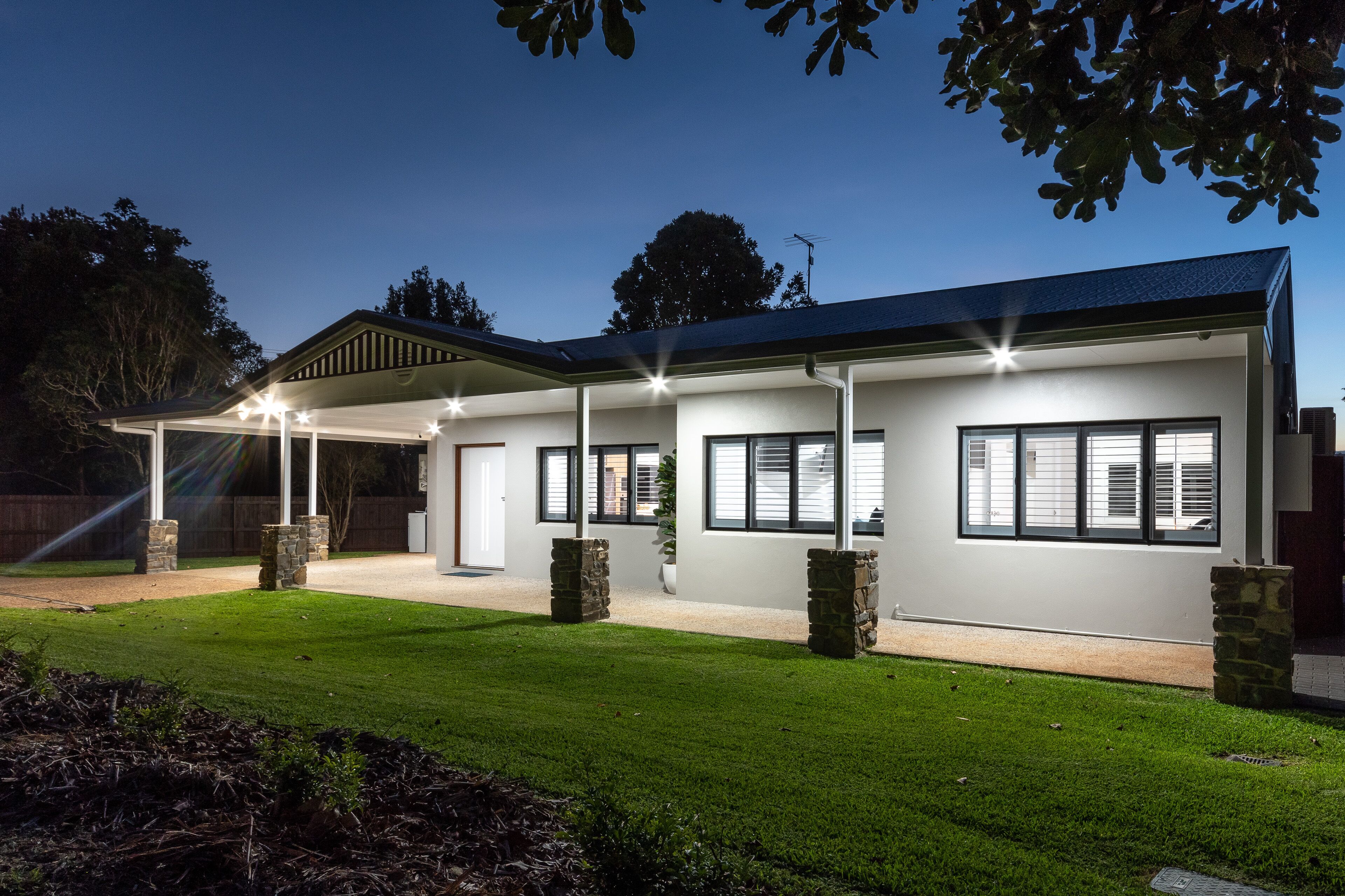 A modern house with a covered patio, stone pillars, and a well-maintained lawn.