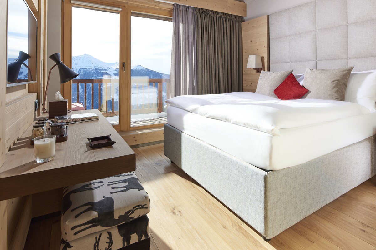 Ein Schlafzimmer mit Bett, Nachttisch, Lampe und Blick auf Berge.