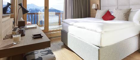 A bedroom with a bed, bedside table, lamp, and a view of mountains.