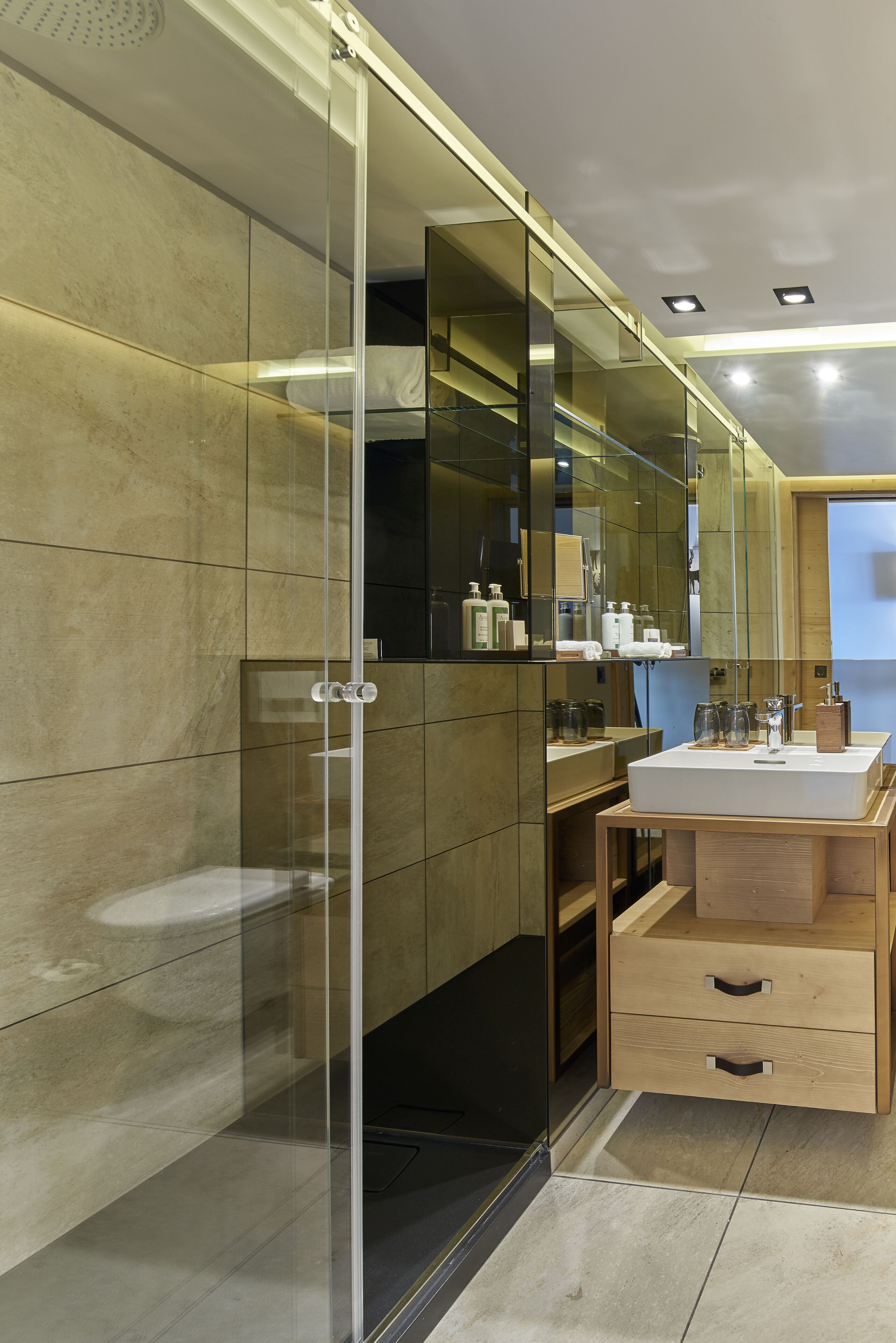 A modern bathroom with a glass shower enclosure, a wooden vanity with a sink, and a large mirror.
