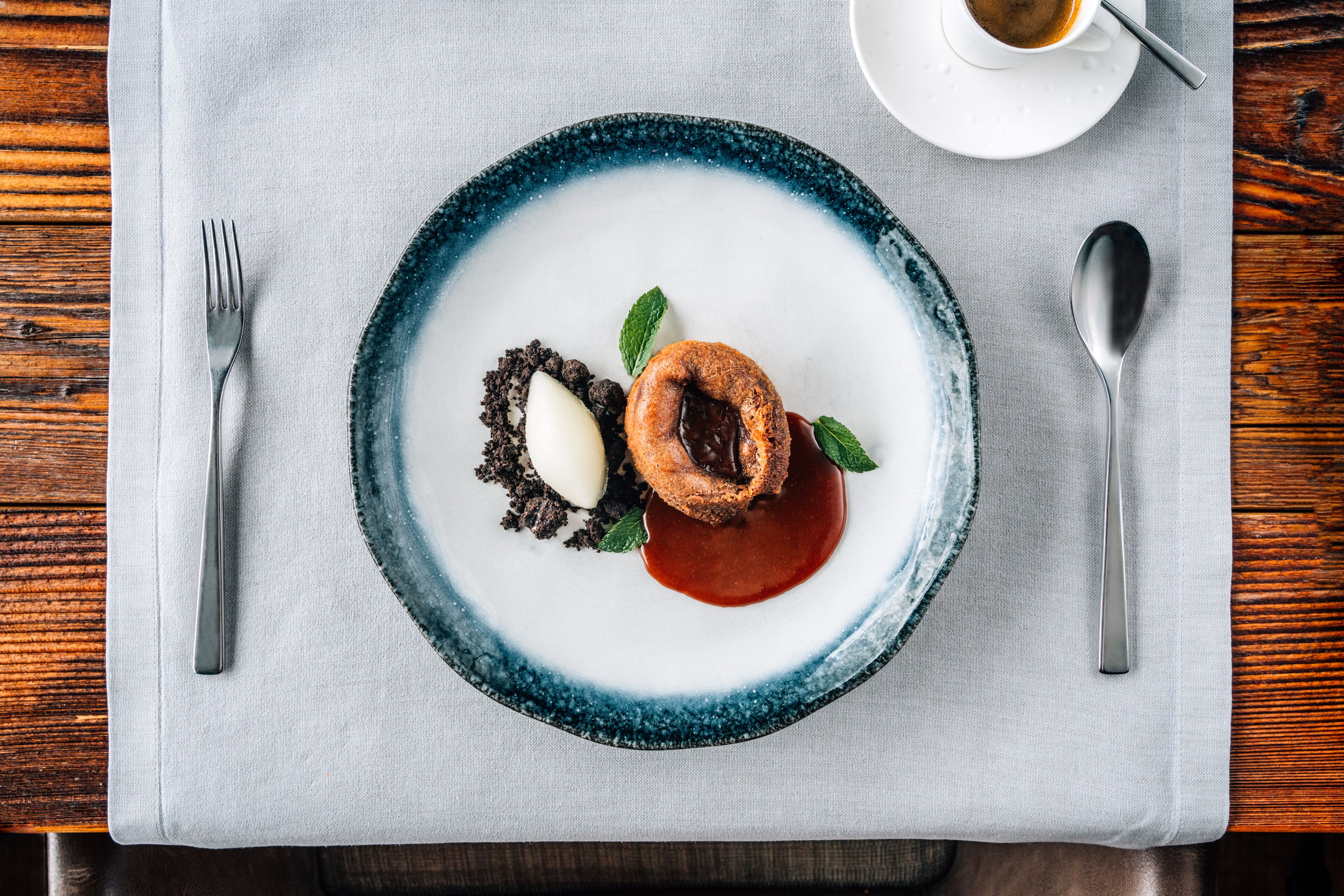 A dessert plate with a chocolate cake, a scoop of ice cream, and a chocolate sauce, placed on a white napkin over a wooden table.