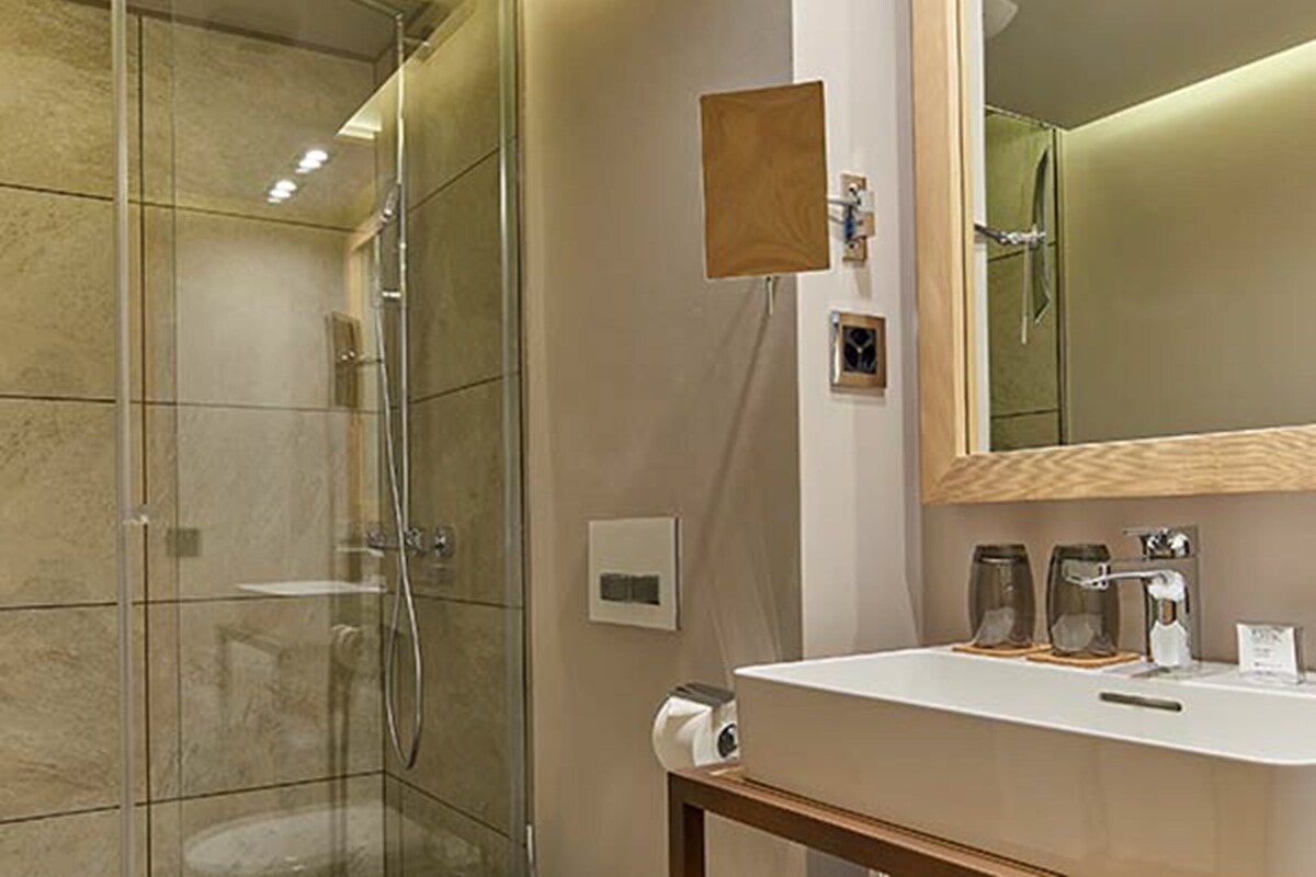 Ein modernes Badezimmer mit einer gläsernen Duschkabine, einem weißen Waschbecken mit Holzablage und einem Spiegel mit Holzrahmen.