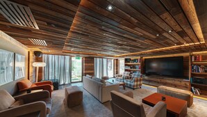 Uma sala de estar ampla com uma televisão de tela grande, assentos confortáveis e teto de madeira.