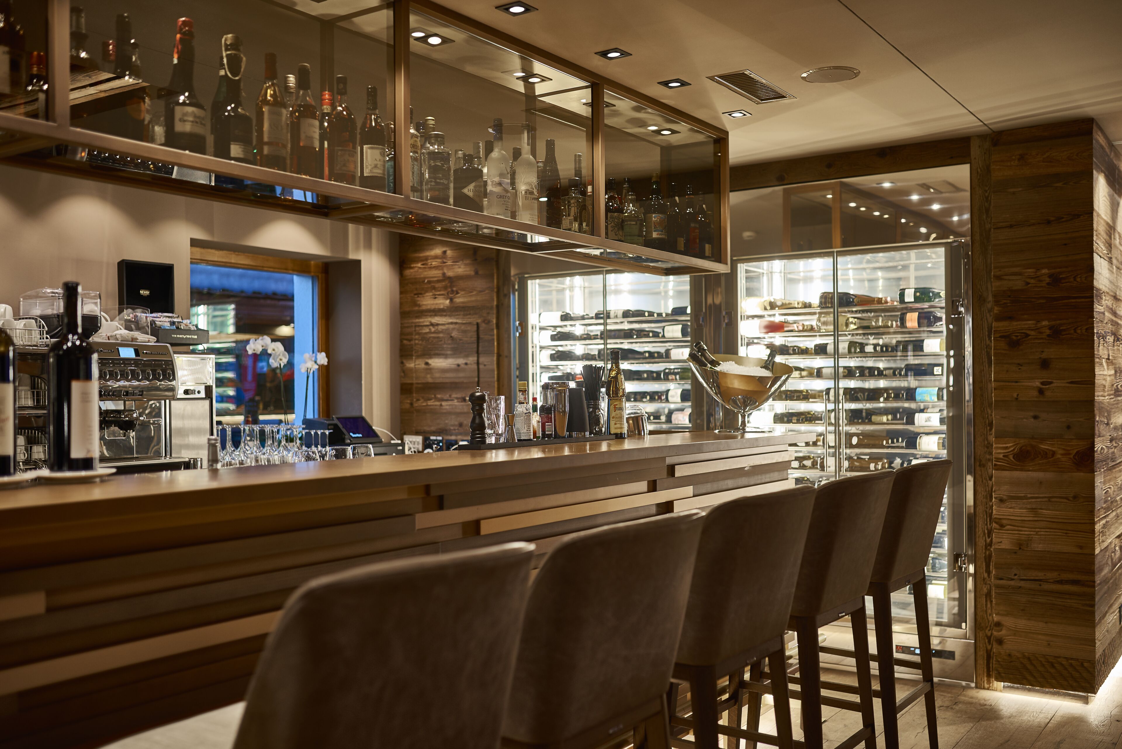 A bar area with a wooden counter, bar stools, and shelves of liquor bottles.