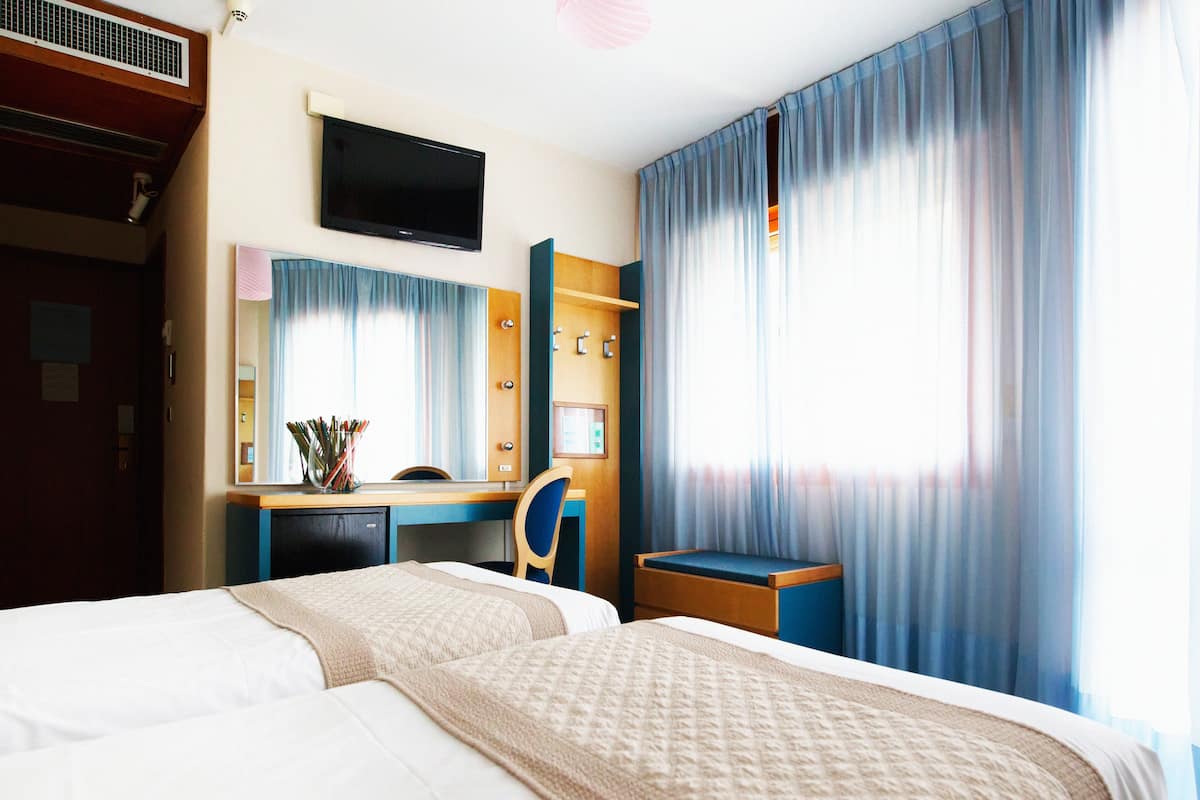 A hotel room with two beds, a desk, a TV, and a bathroom.