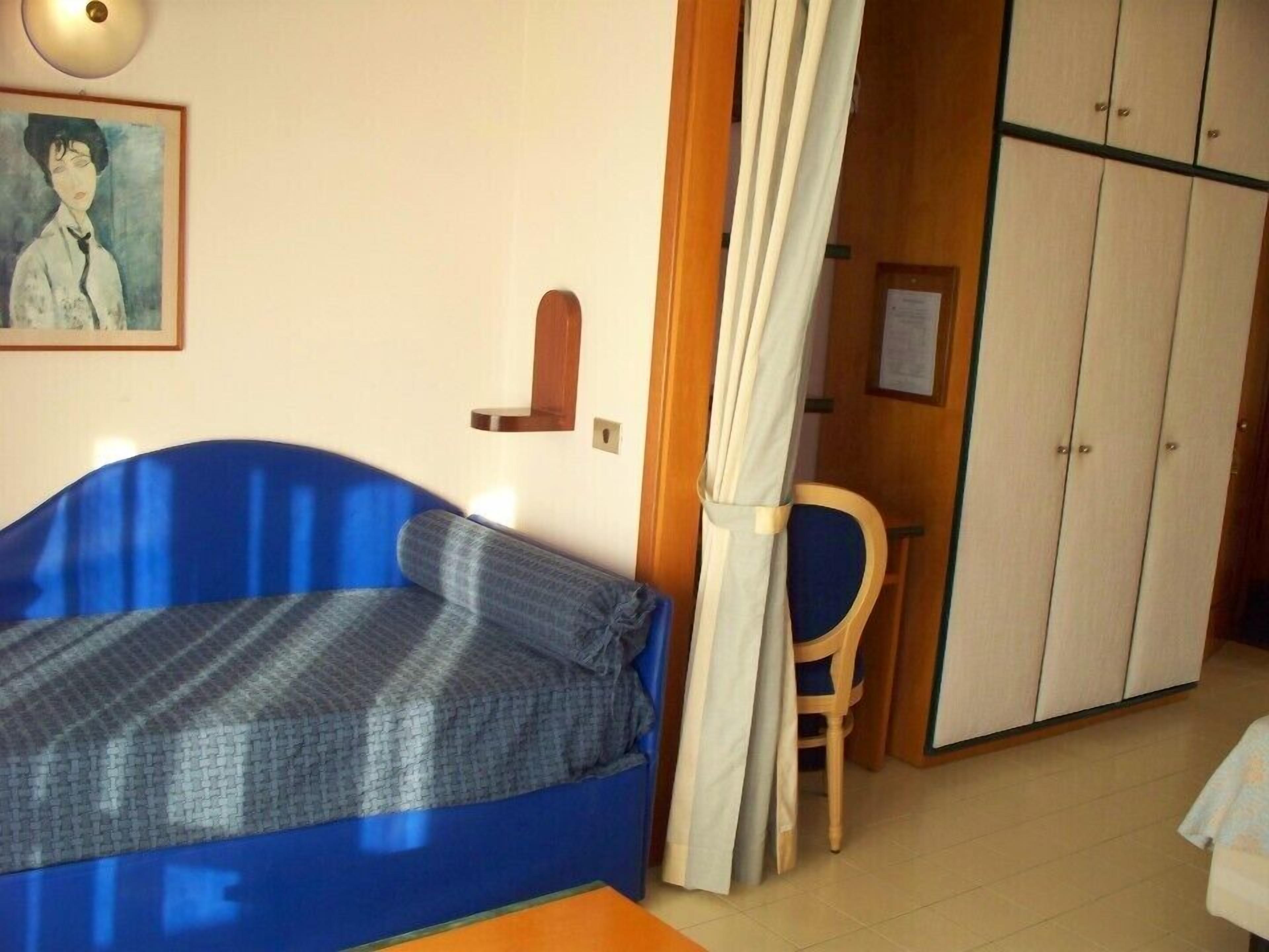 Ein Zimmer mit einem blauen Sofa, einem Holzstuhl, einem Kleiderschrank und einem Bild an der Wand.