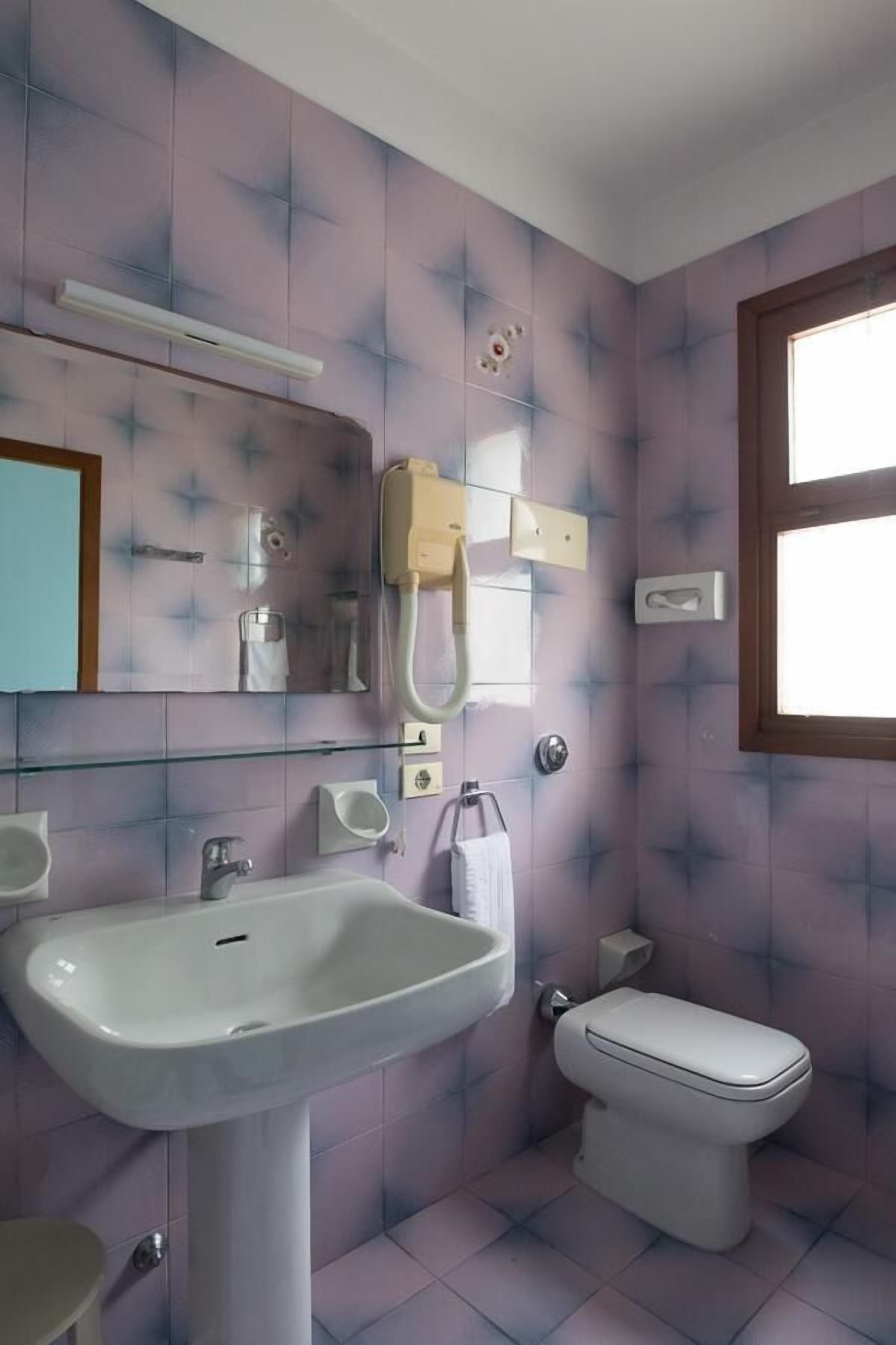 A bathroom with a pedestal sink, a toilet, and a mirror.