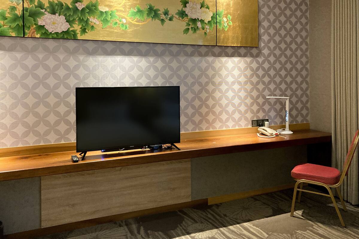 A modern room with a flat-screen TV on a wooden desk, a chair, and a decorative wall panel above.