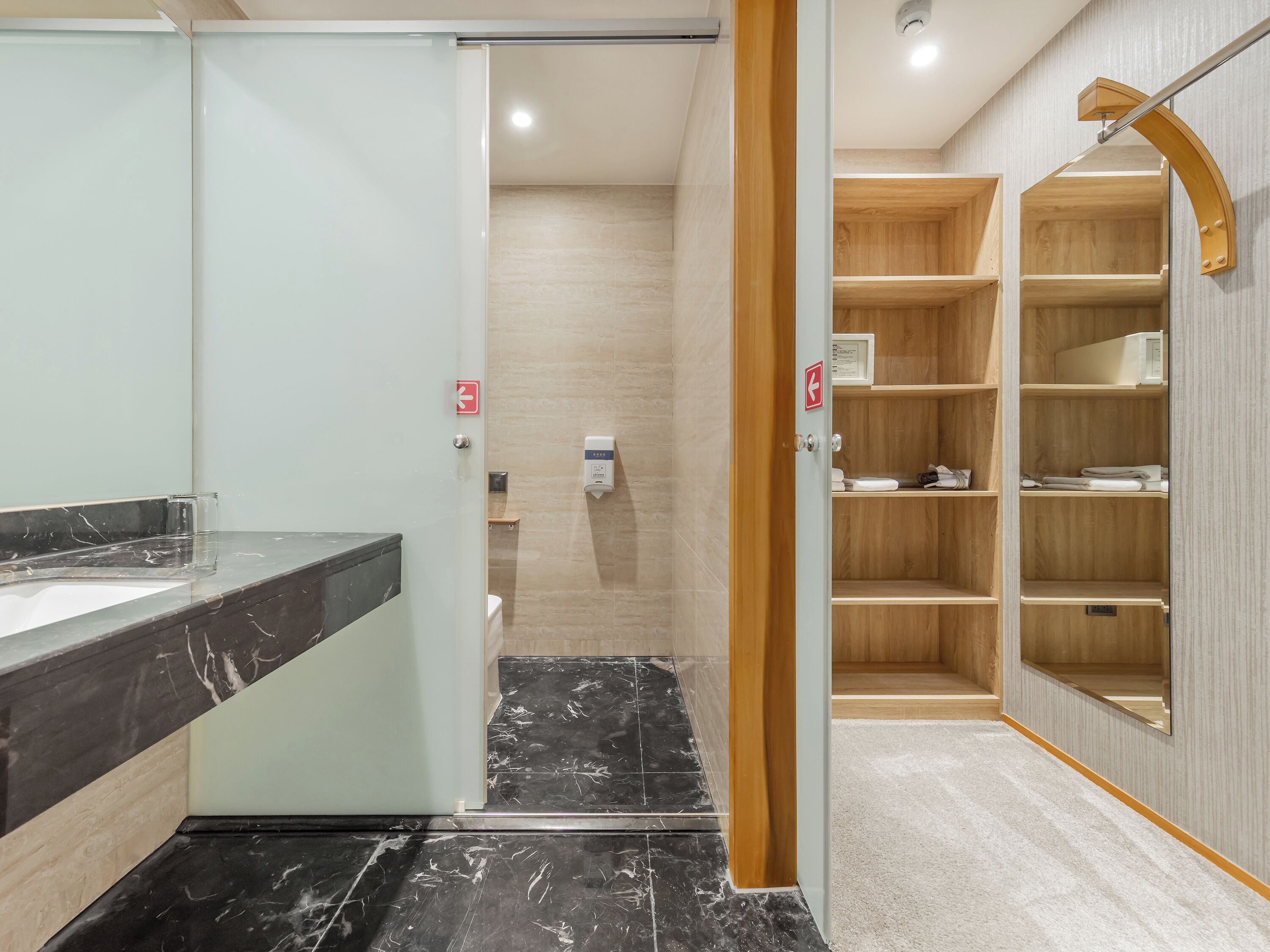 Un baño con encimera de mármol, inodoro, secamanos y estante de madera.