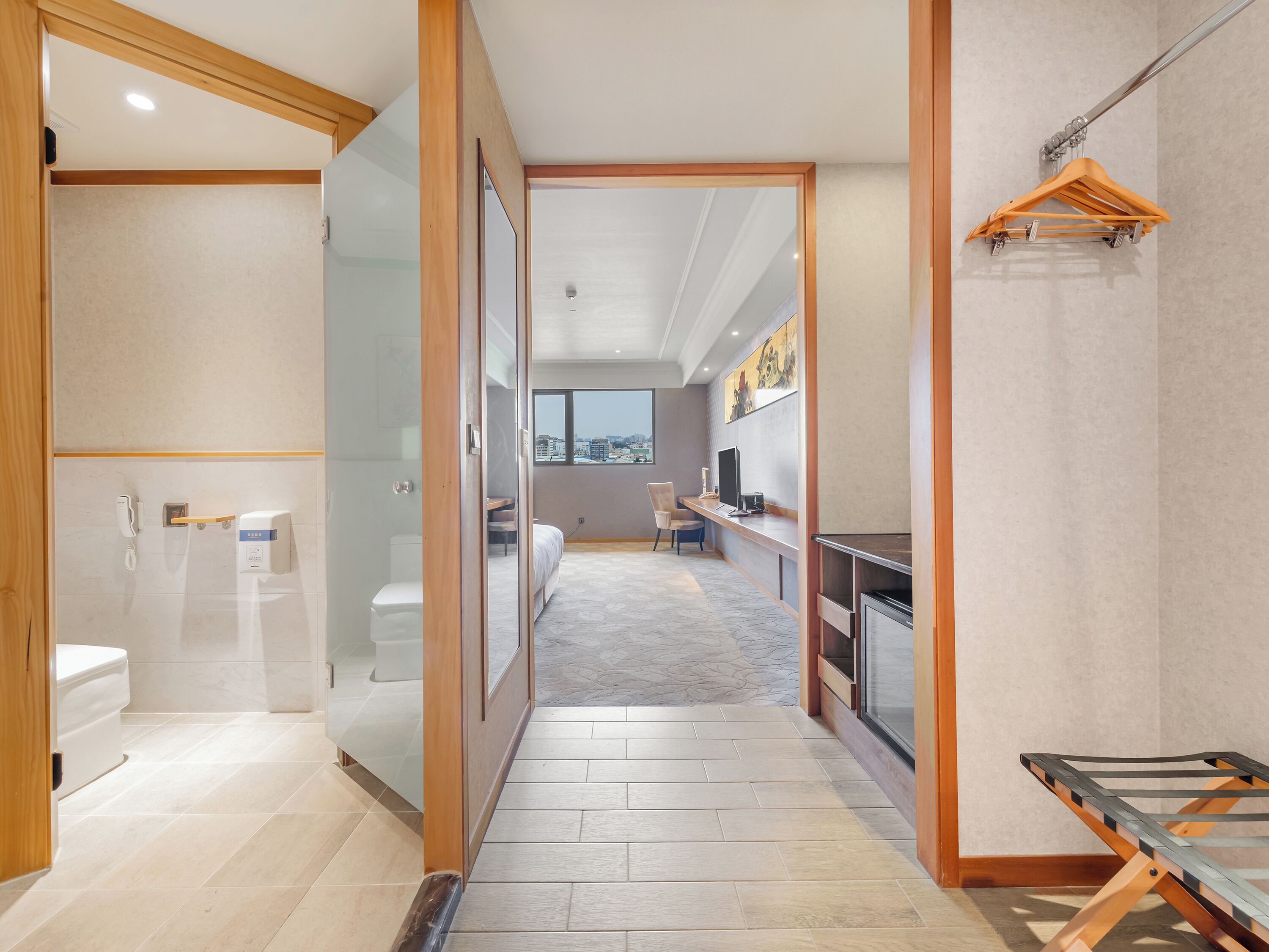 Habitación de hotel moderna con baño, pasillo que conduce a un dormitorio y vista de la ciudad.