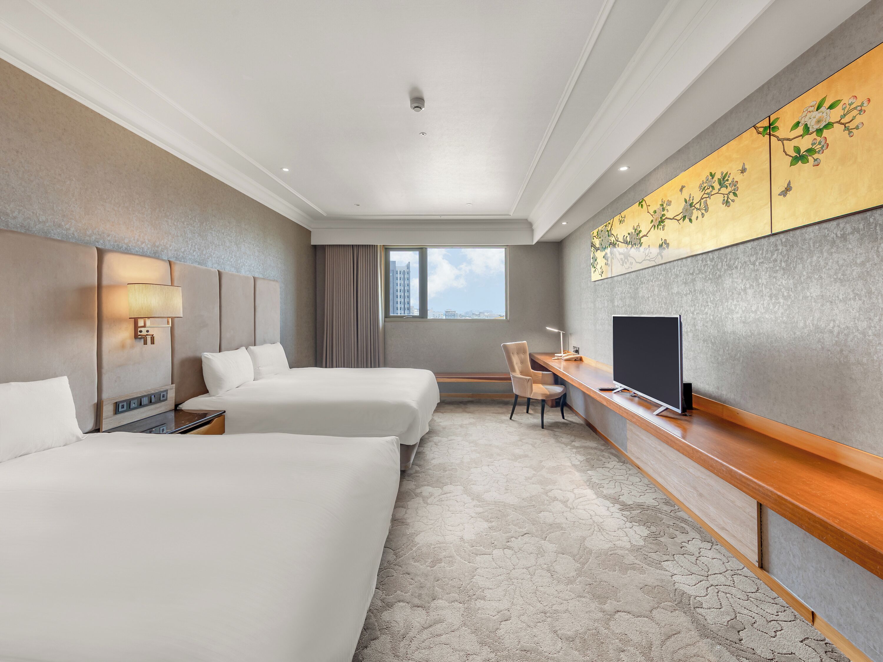 A hotel room with two beds, a desk, a TV, and a large window.