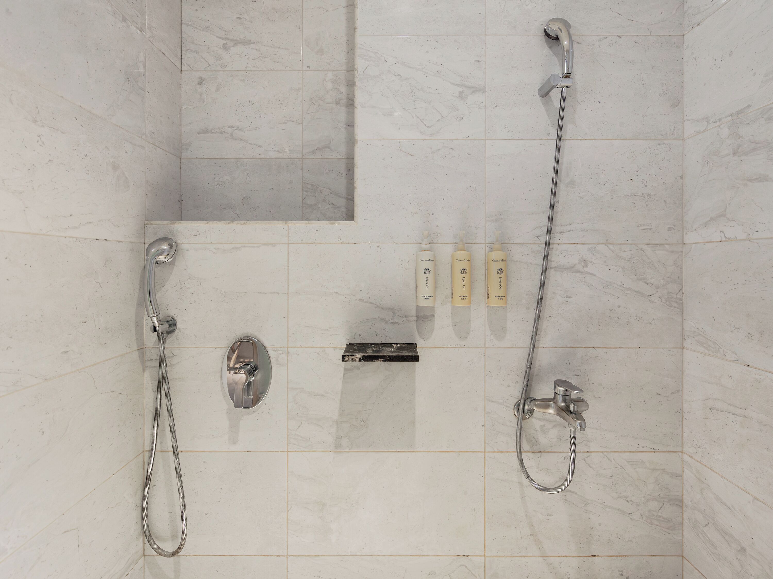Un baño con dos cabezales de ducha, una ducha de mano y tres botellas de champú.