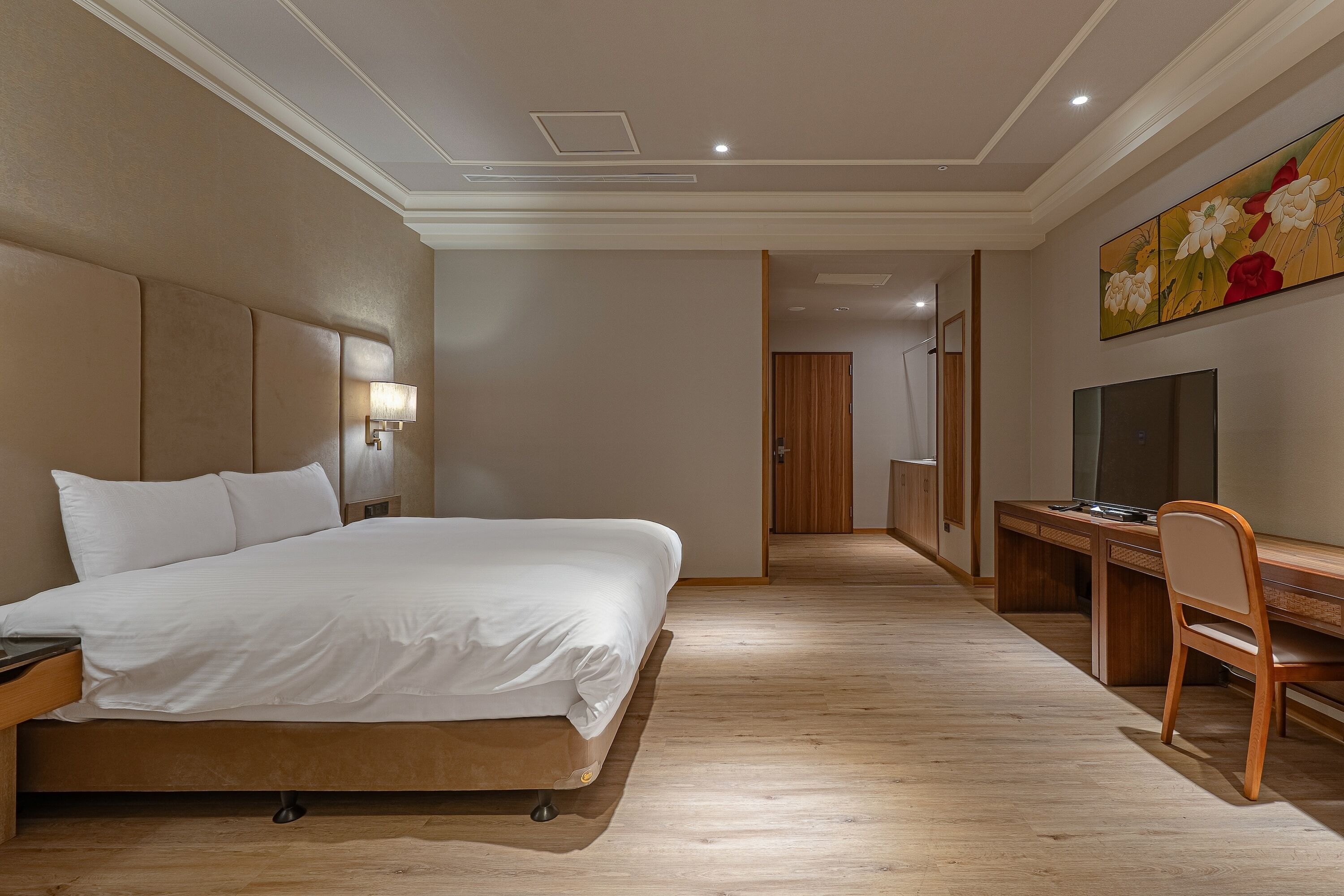 Habitación de hotel con una cama grande, un escritorio con silla, un televisor y un cuadro en la pared.