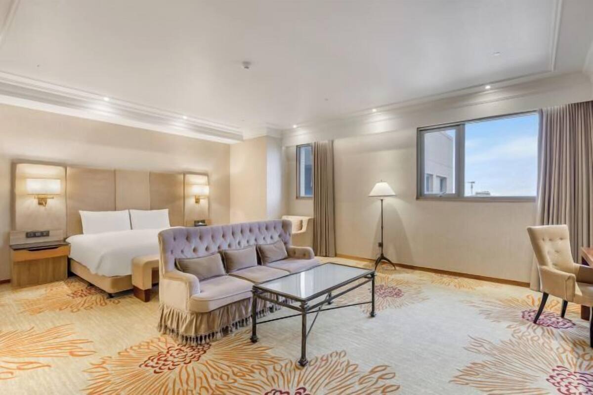 A hotel room with a bed, a sofa, a coffee table, a desk, and a lamp.