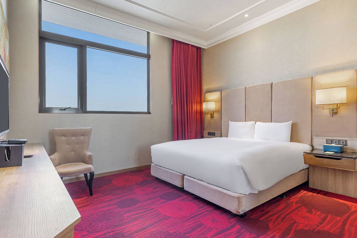 A hotel room with a large bed, a desk with a chair, a TV, and a window with curtains.