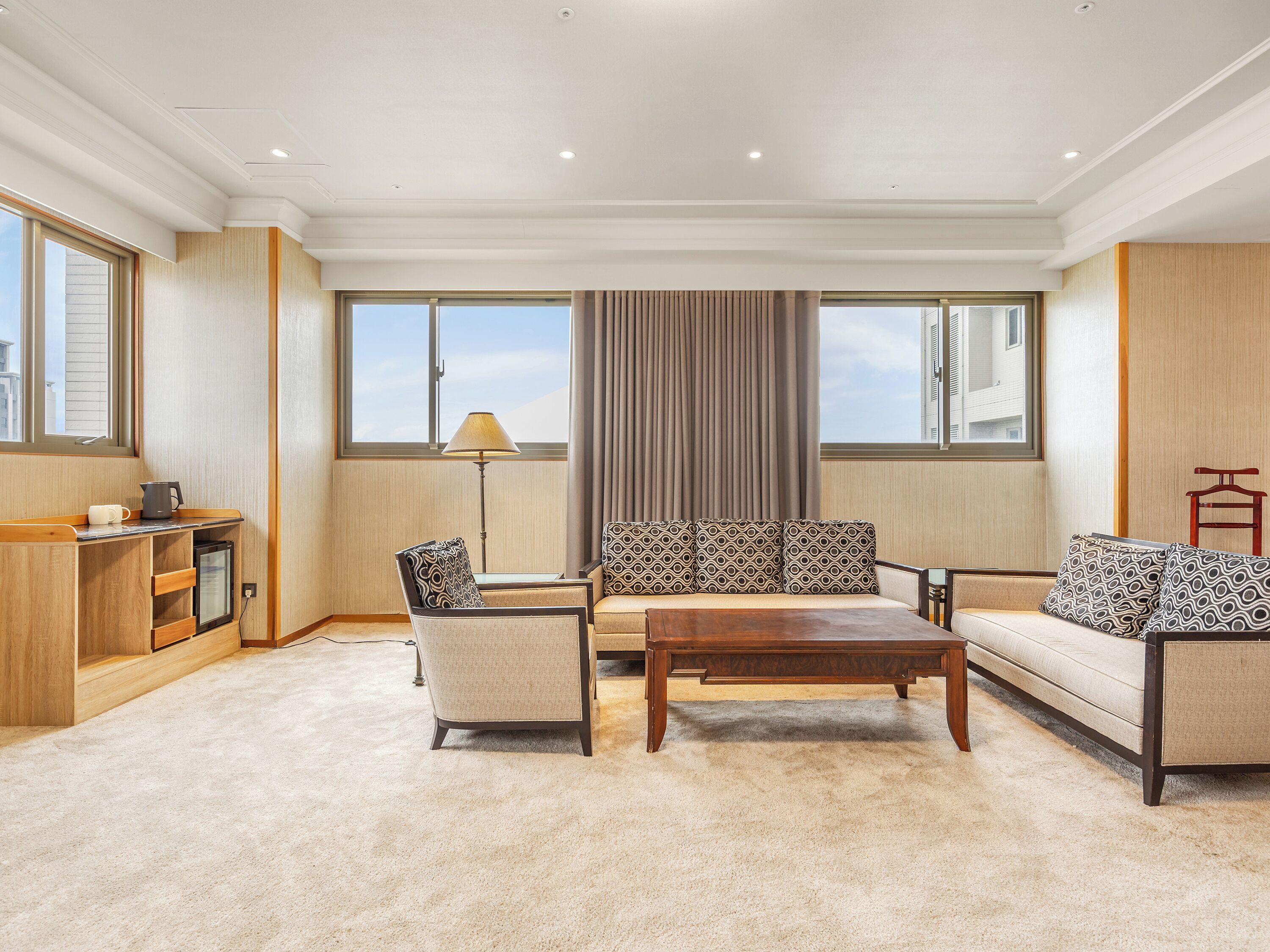 A modern living room with a sofa set, a coffee table, and a side table. There is a lamp, a small cabinet, and a window with curtains.