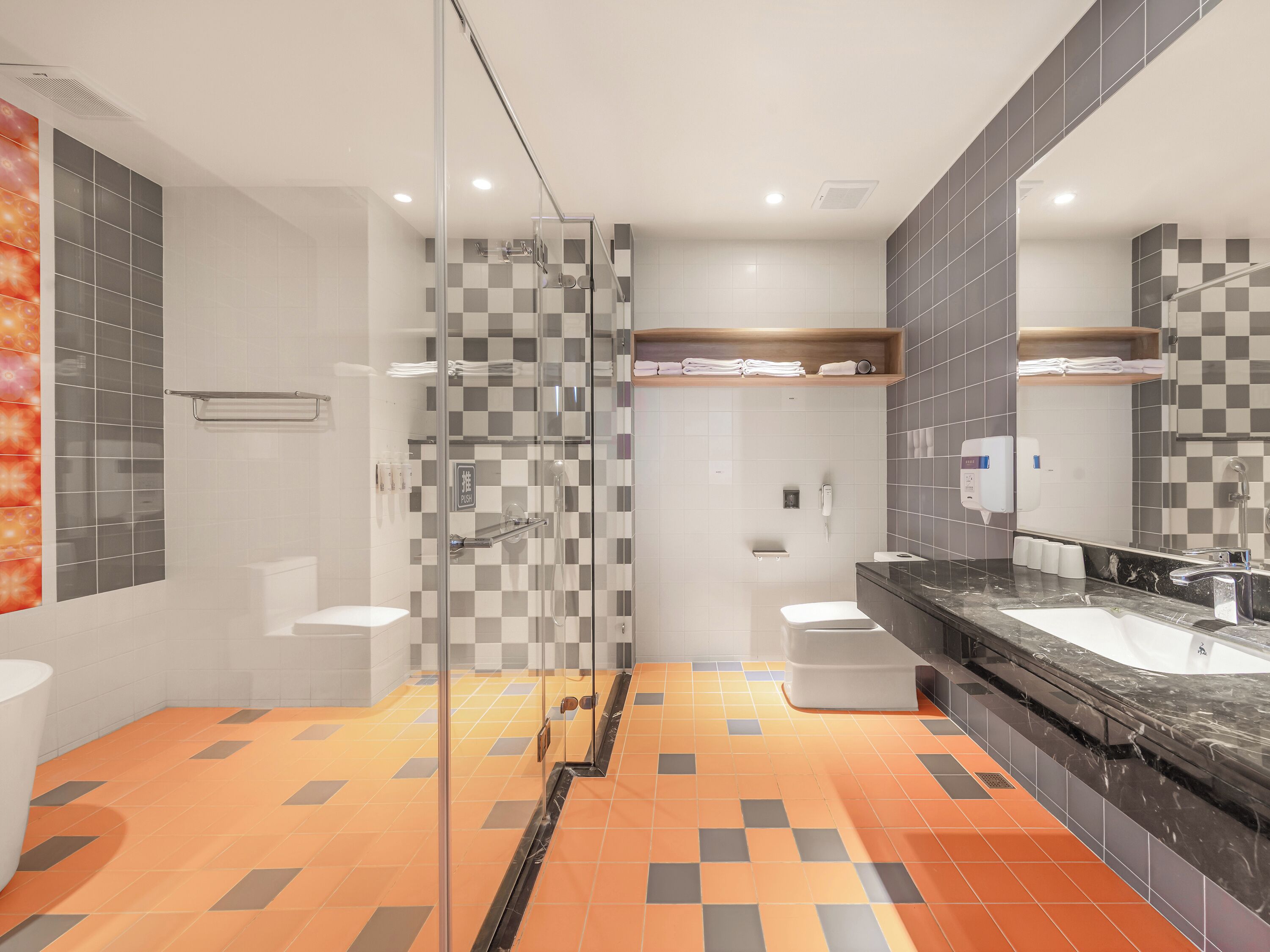 A modern bathroom with a glass shower enclosure, a vanity with a black marble countertop, and checkered tile flooring.