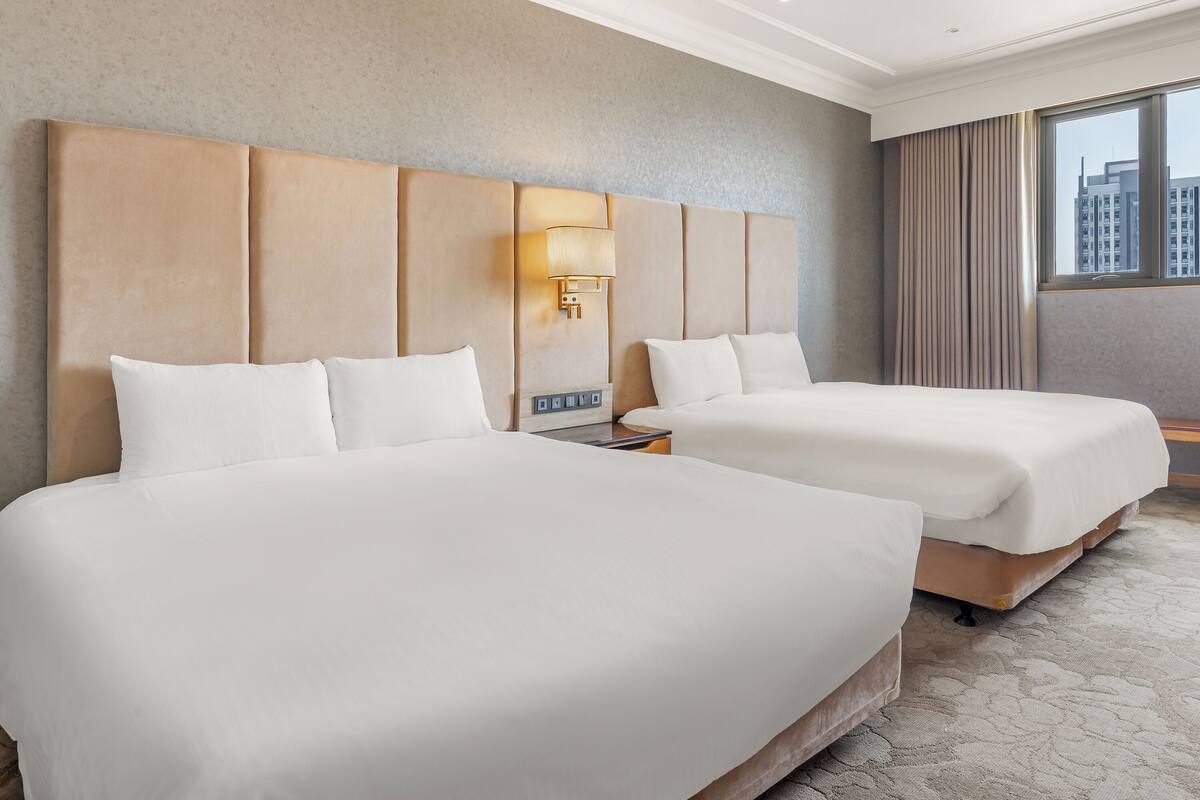 A hotel room with two beds, a large window, and a city view.