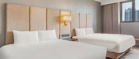 A hotel room with two beds, a large window, and a city view.