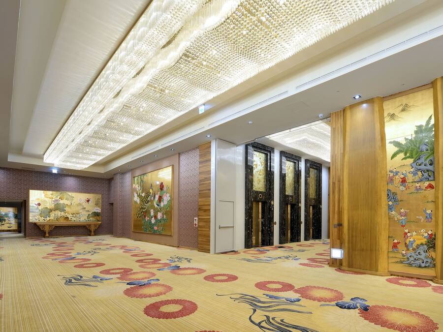 Um hall de hotel espaçoso com carpete estampado, uma grande pintura na parede e um tradicional biombô de madeira com arte.