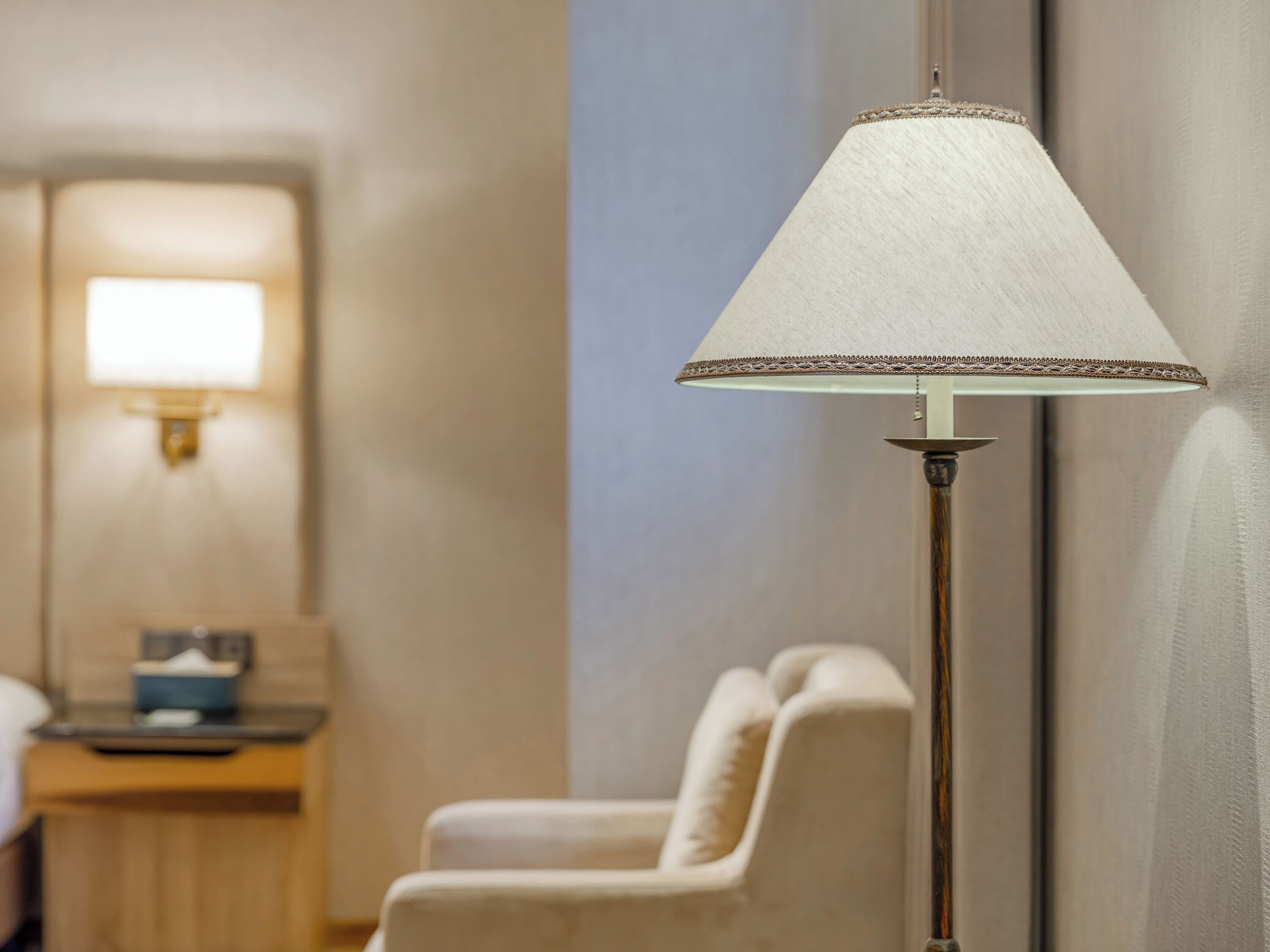 A hotel room with a bedside lamp, a bedside table, and a chair.