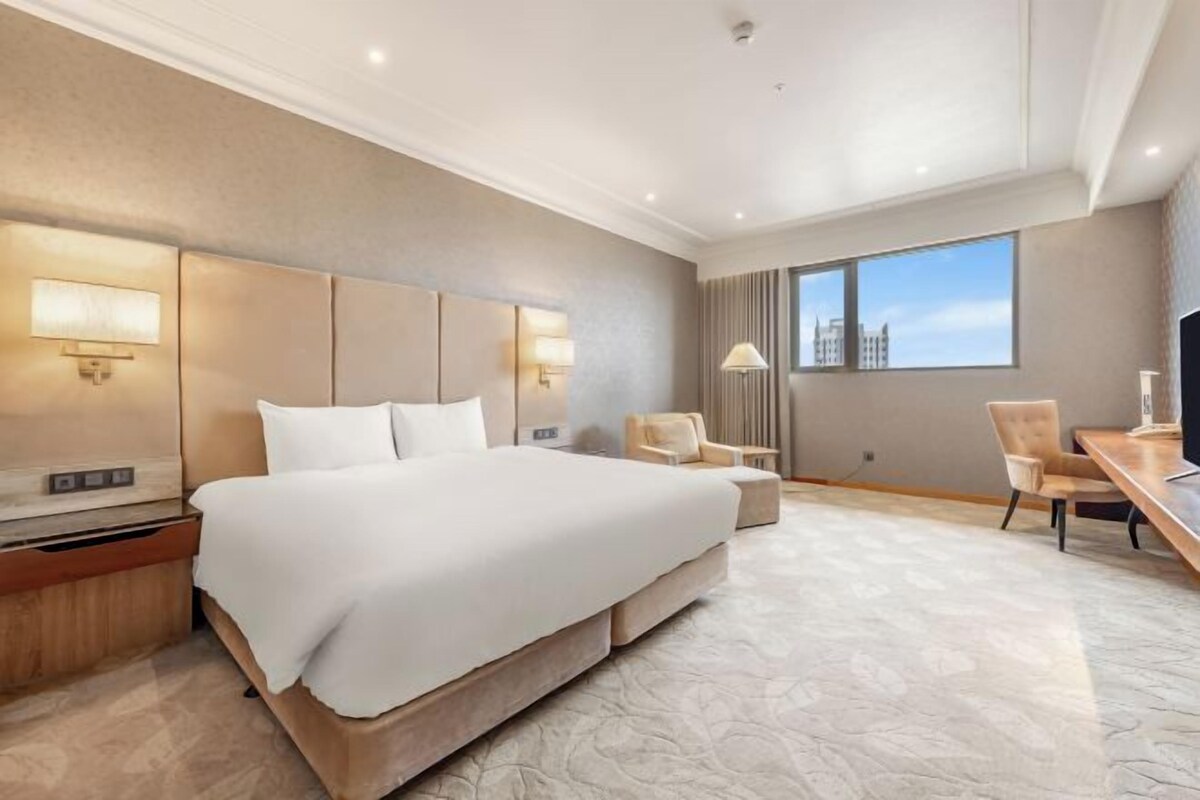 A hotel room with a large bed, bedside tables, a desk, and a chair.