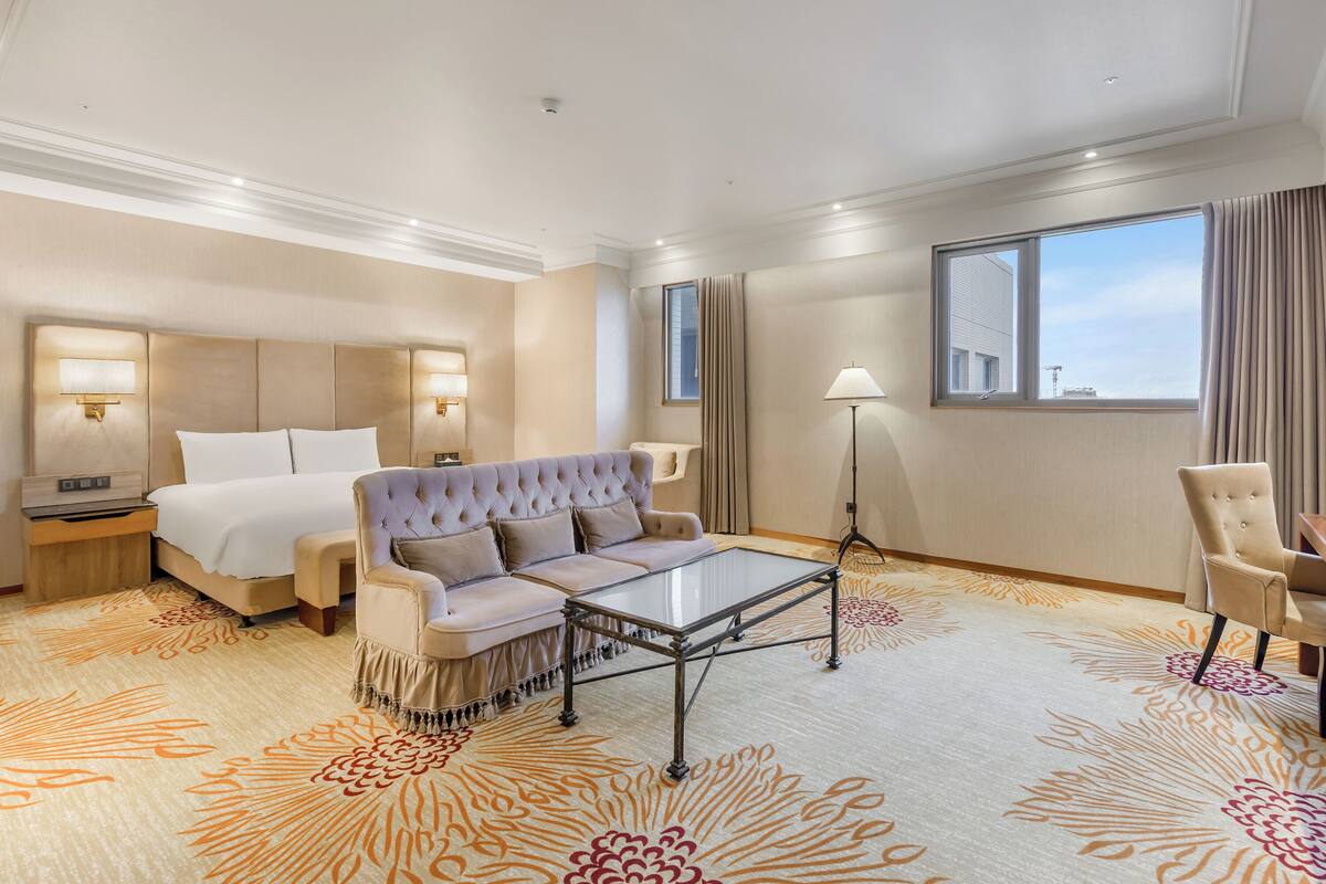A hotel room with a bed, a sofa, a coffee table, a desk, and a chair.