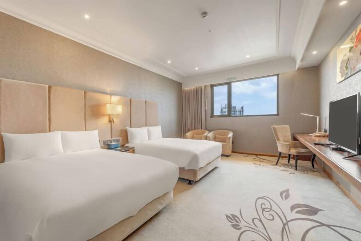 A hotel room with two beds, a desk, a chair, a TV, and a large window.