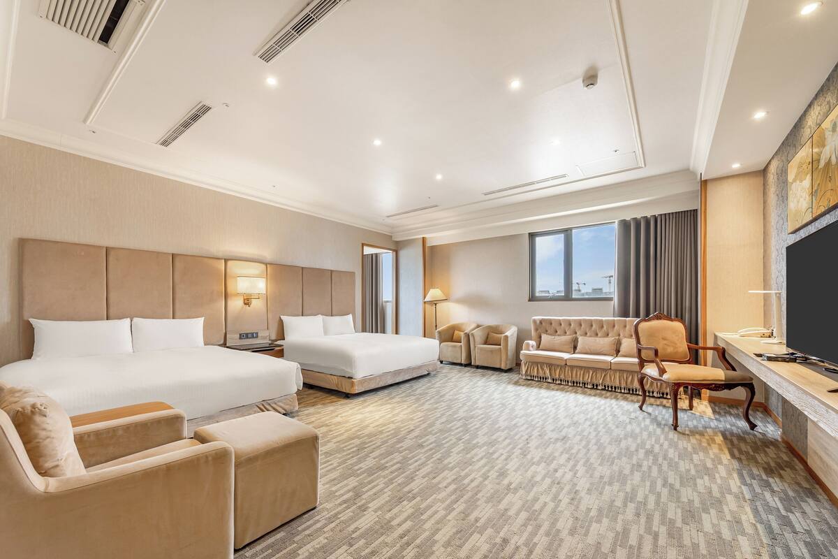 A hotel room with a large bed, two armchairs, a sofa, a desk, and a TV.