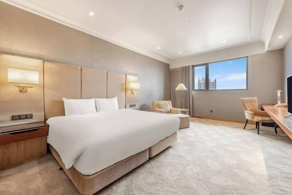 A hotel room with a large bed, bedside tables, a desk, and a chair.
