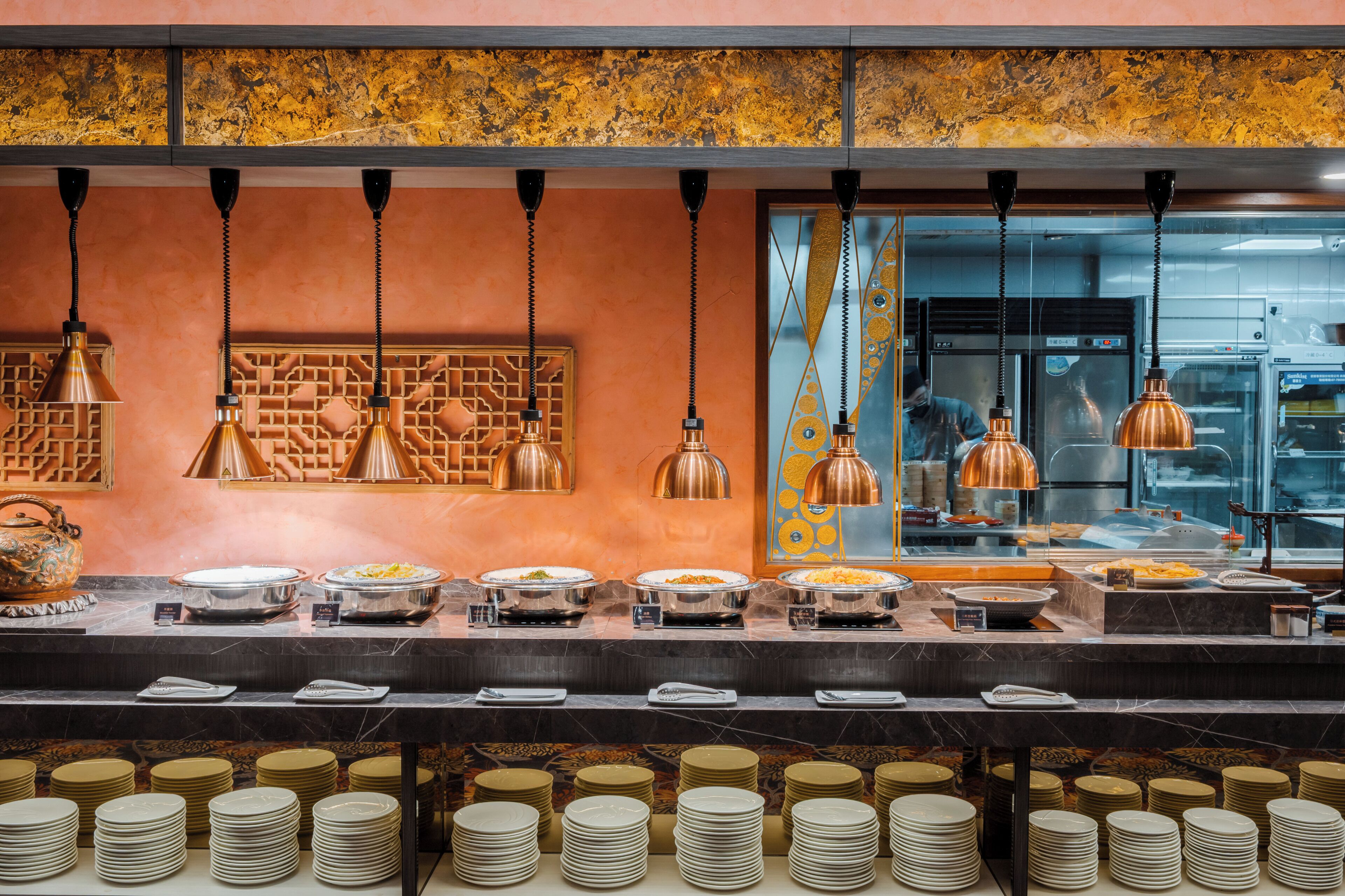 A buffet setup with multiple serving stations, a marble countertop, and hanging copper pendant lights.