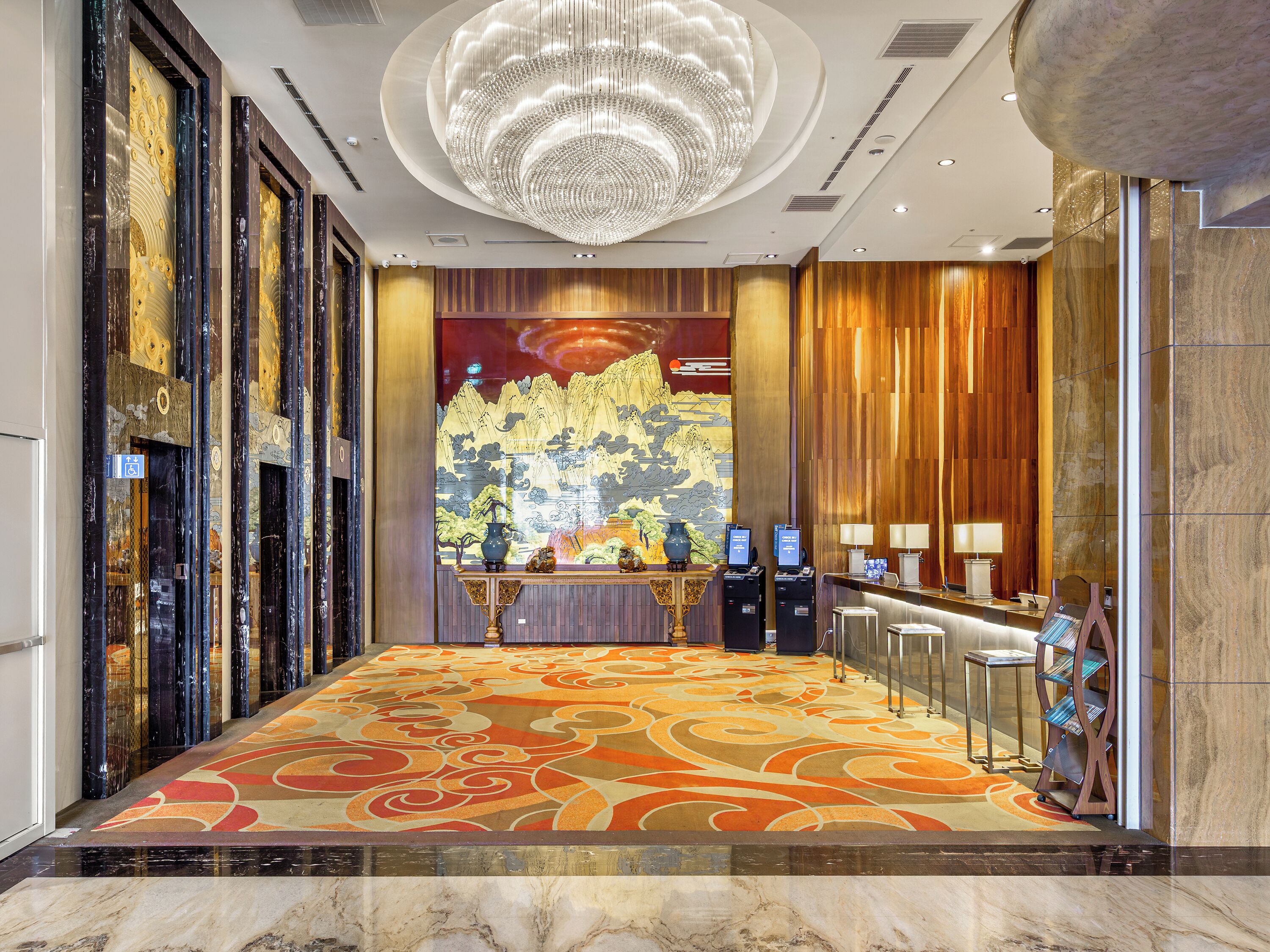 A hotel lobby with a marble floor, a large chandelier, a reception desk, and a mural on the wall.