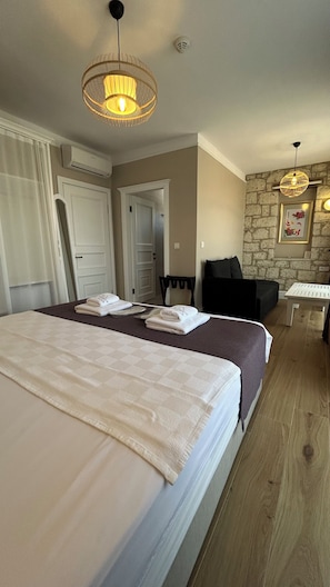 A hotel room with a large bed, a desk, a chair, a stone wall, and two hanging lamps. - Vodina Alaçatı (Cesme)