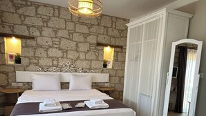 Ein Hotelzimmer mit einer Steinwand, einem großen Bett, einer hängenden Leuchte und einem Holzboden.