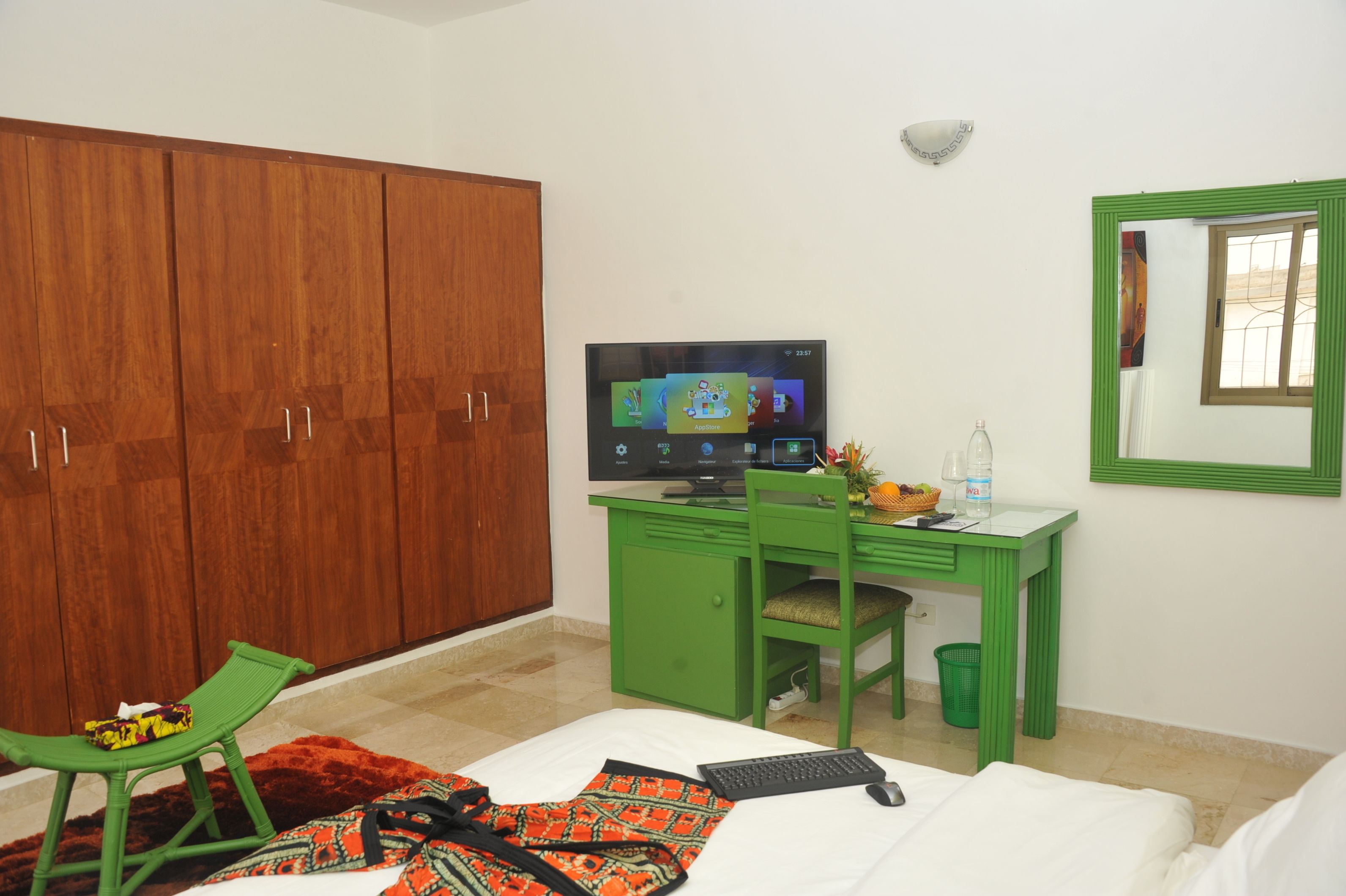 Een kamer met een houten garderobe, een groen bureau met een computer, een stoel en een bed met een witte dekbedovertrek.