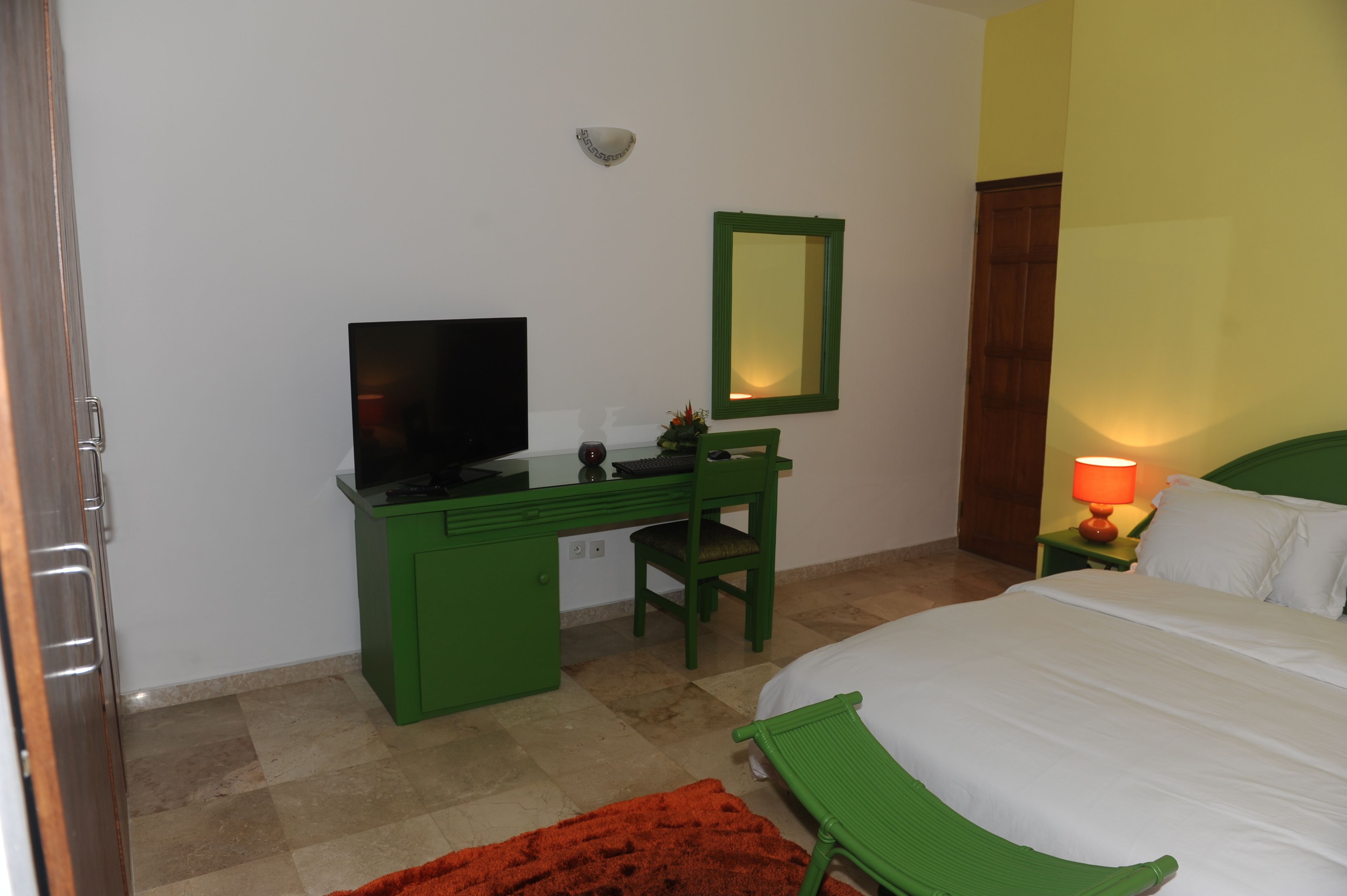 Una habitació amb un llit, escriptori amb televisió, una cadira, una làmpada i un mirall.