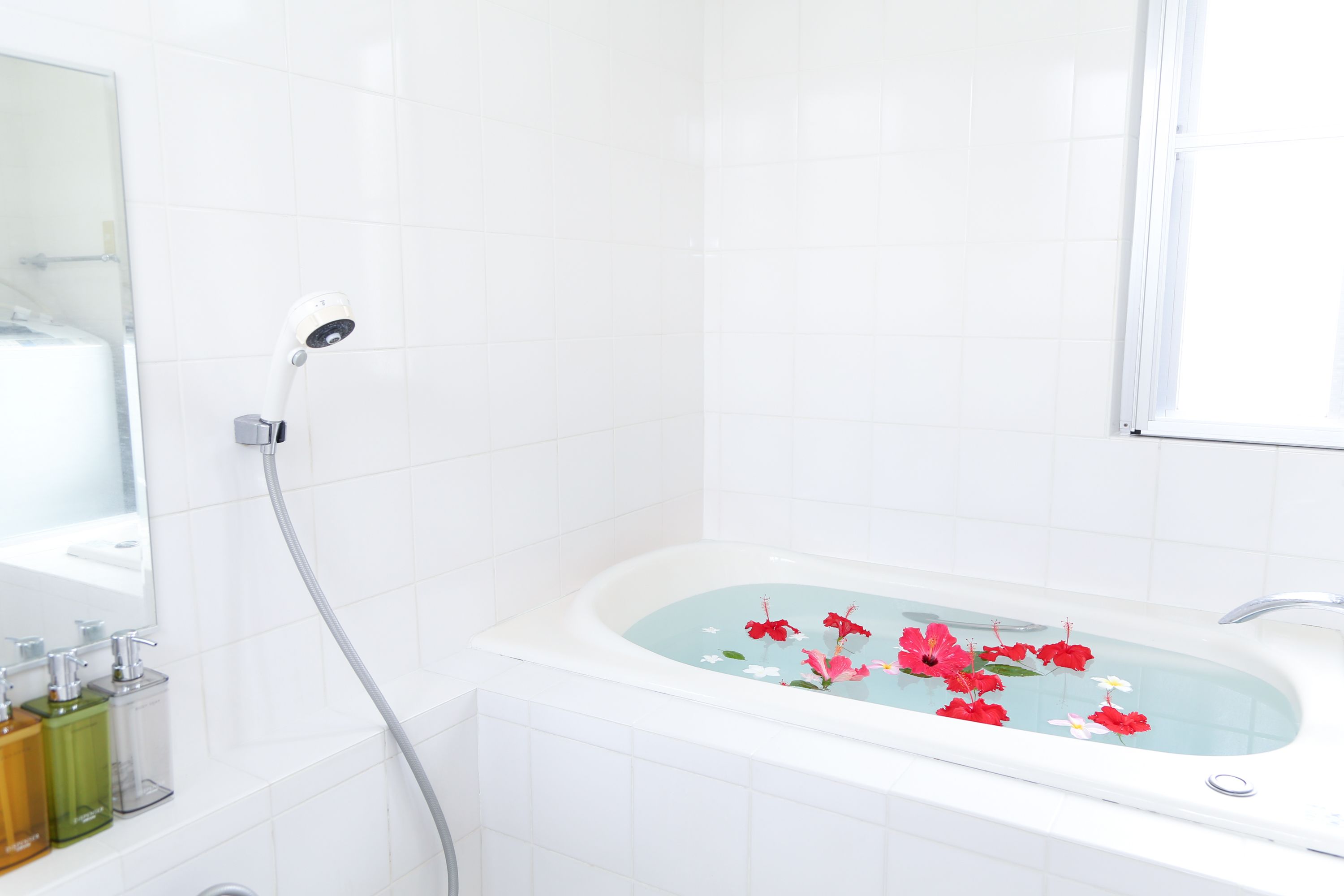 A bathroom with a bathtub filled with water and floating flowers, a showerhead, and a mirror.