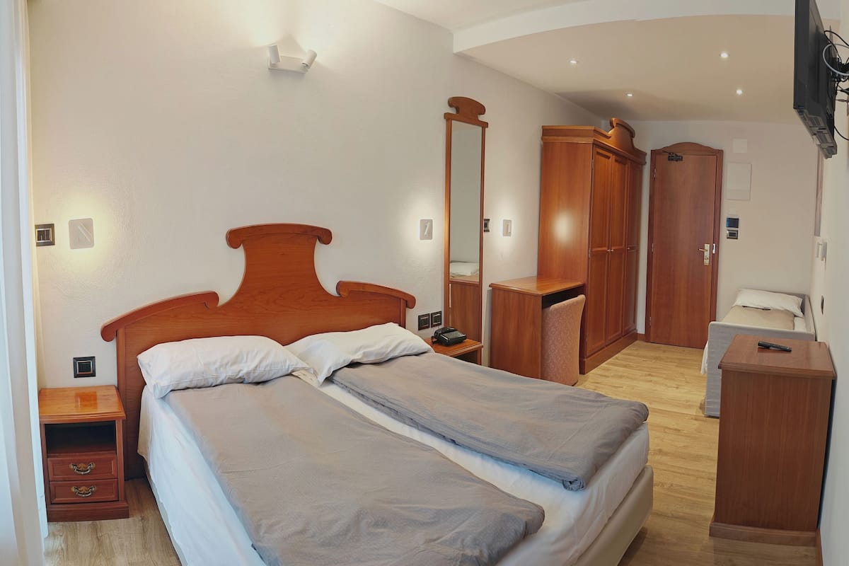 A bedroom with a double bed, wooden wardrobe, and a nightstand with a lamp.