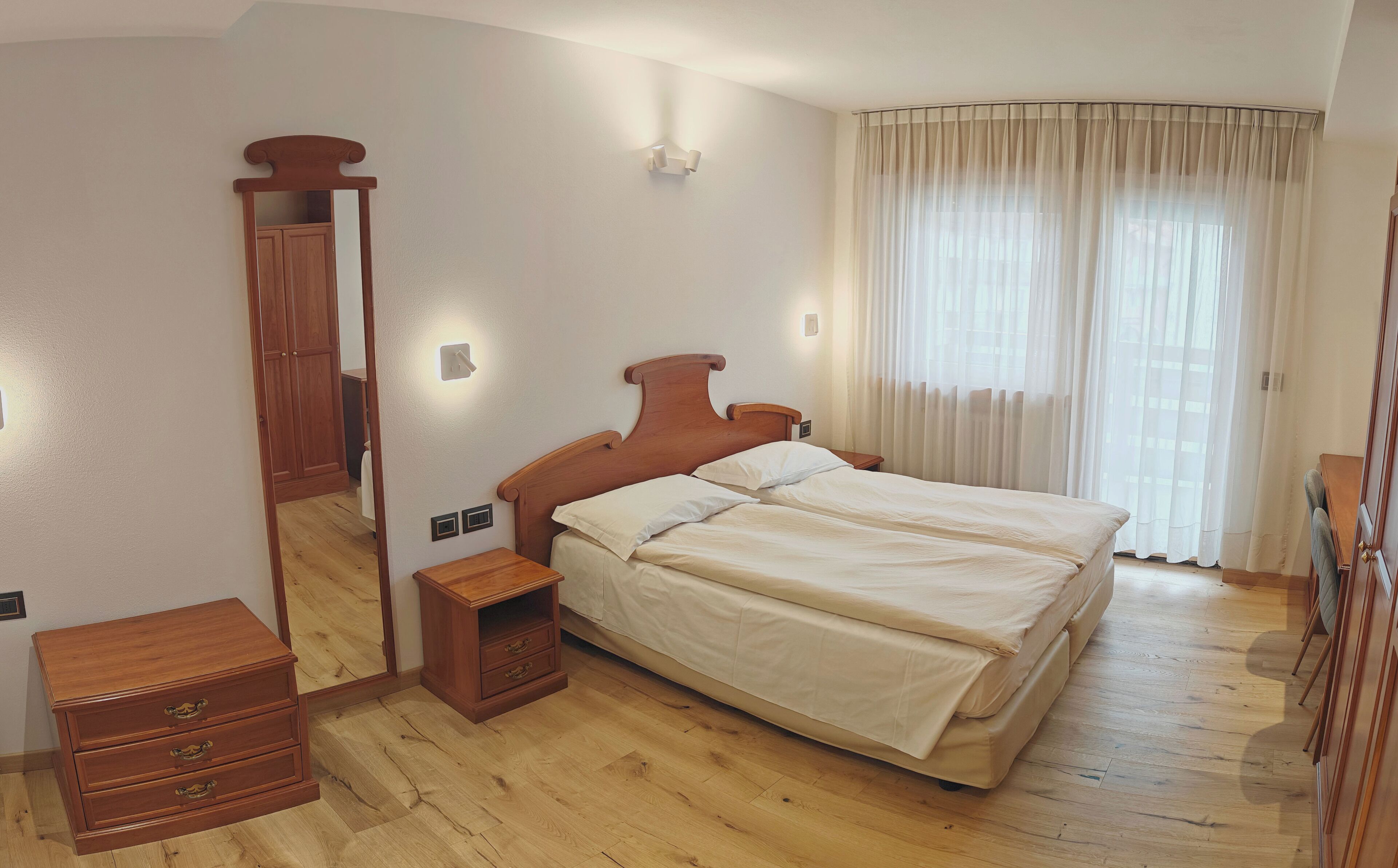 A bedroom with a wooden bed, a nightstand, a dresser, and a large window with curtains.