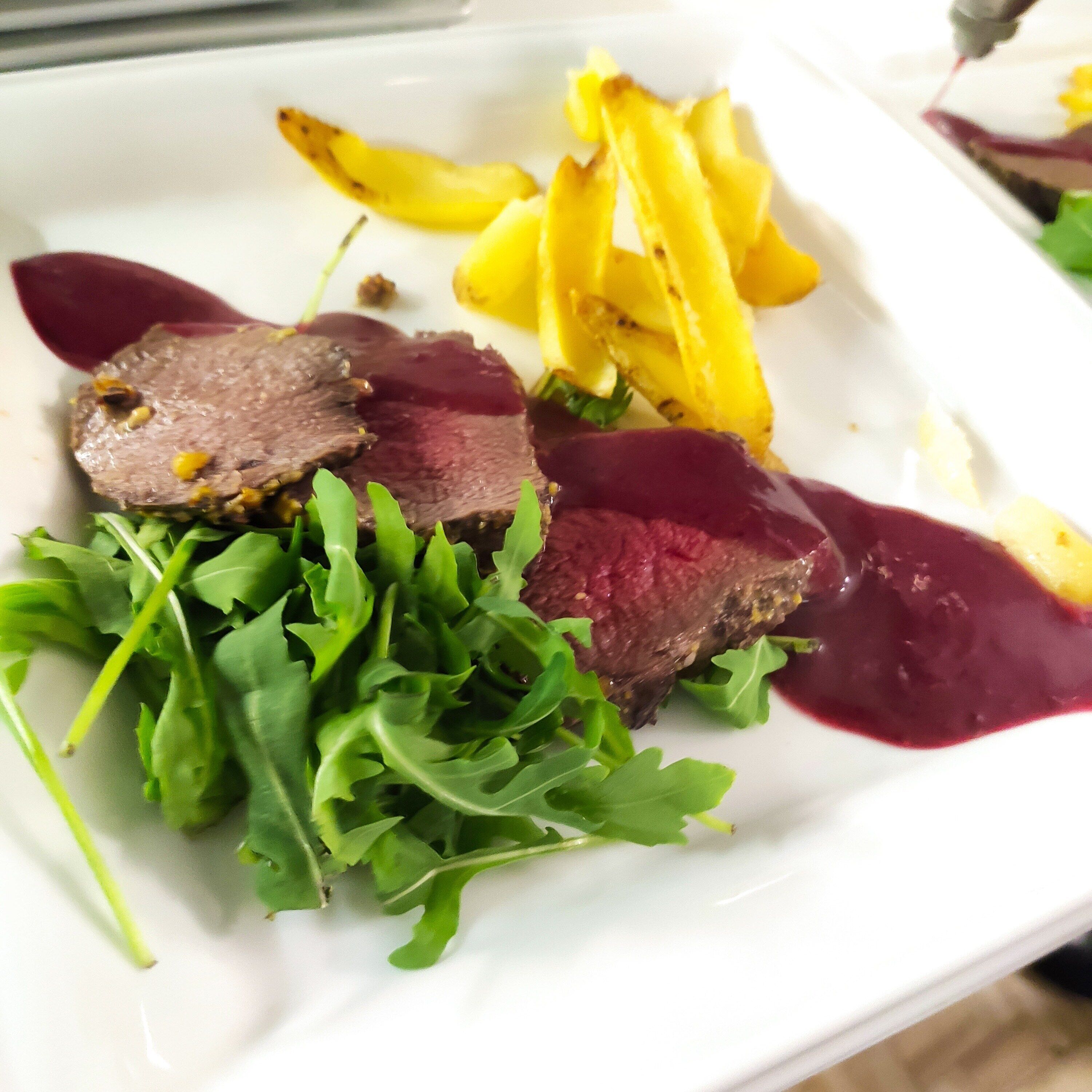 A plate with sliced meat, roasted potatoes, and greens.