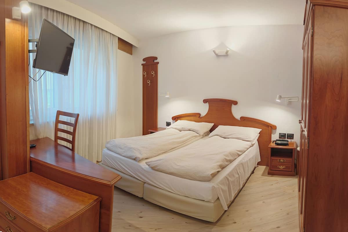 A hotel room with a bed, a desk, a chair, a TV mounted on the wall, a nightstand, and a wardrobe.