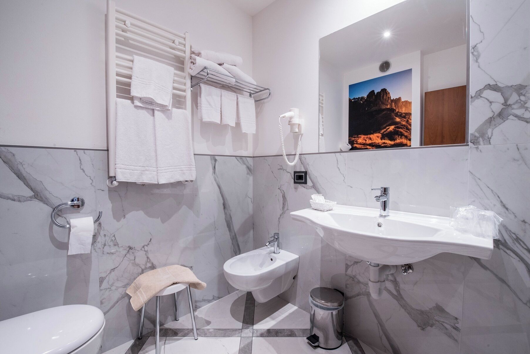 Un baño moderno con pared de mármol, un lavamanos, un bidé y un inodoro.