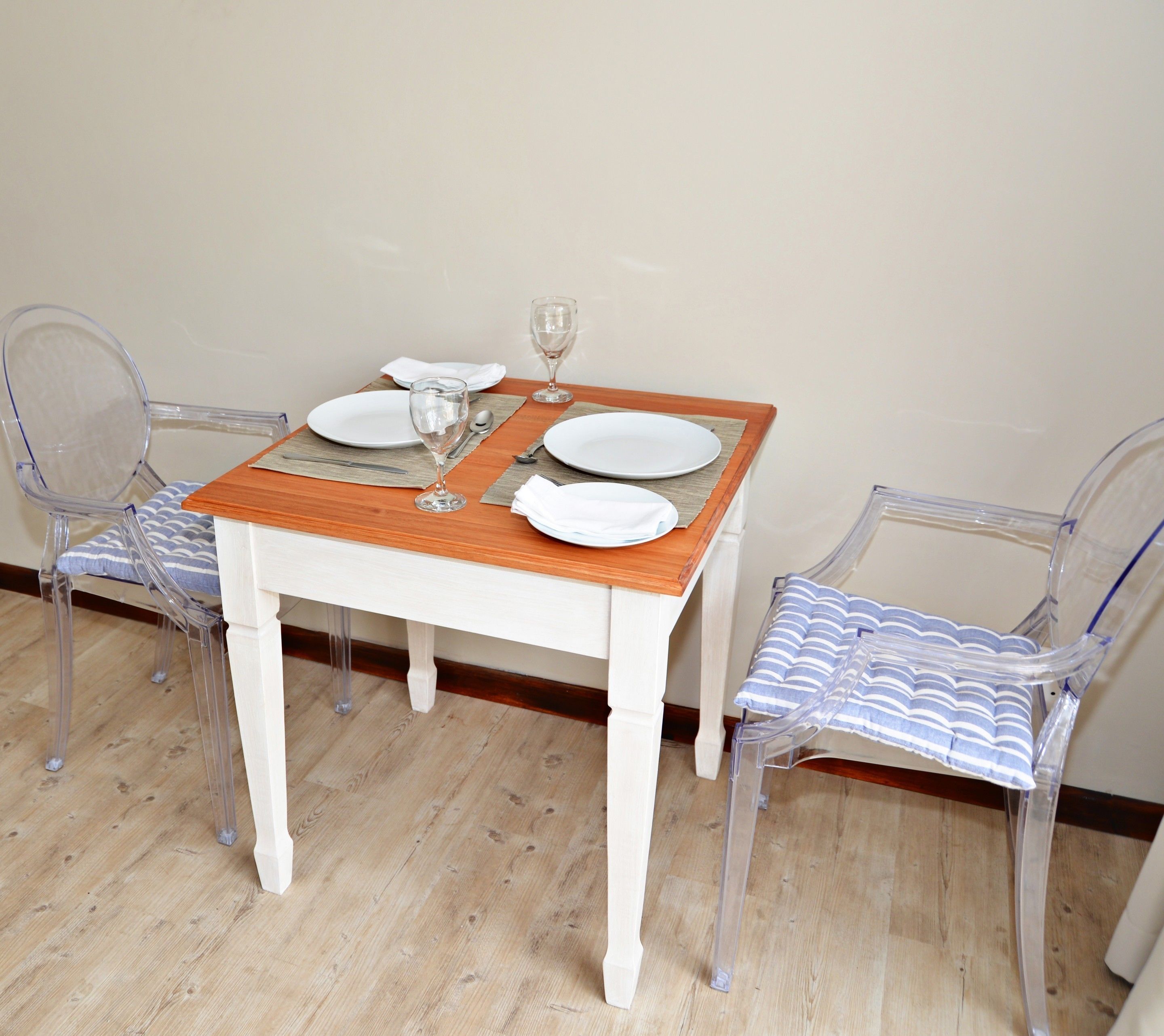 A dining table set with plates, a wine glass, and cutlery, flanked by two transparent chairs with striped cushions.
