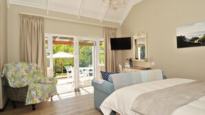 Quarto com cama grande, TV fixada na parede e porta de vidro deslizante para um pátio externo com mesa e cadeiras.