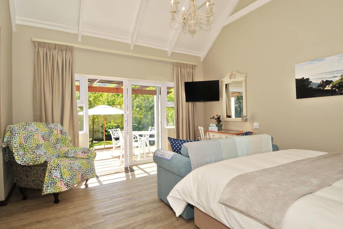 Un dormitorio con una cama grande, un televisor montado en la pared y un ventanal corredero que da a un patio exterior con una mesa y sillas.