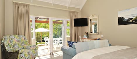 A bedroom with a large bed, a TV mounted on the wall, and a sliding glass door leading to an outdoor patio with a table and chairs.