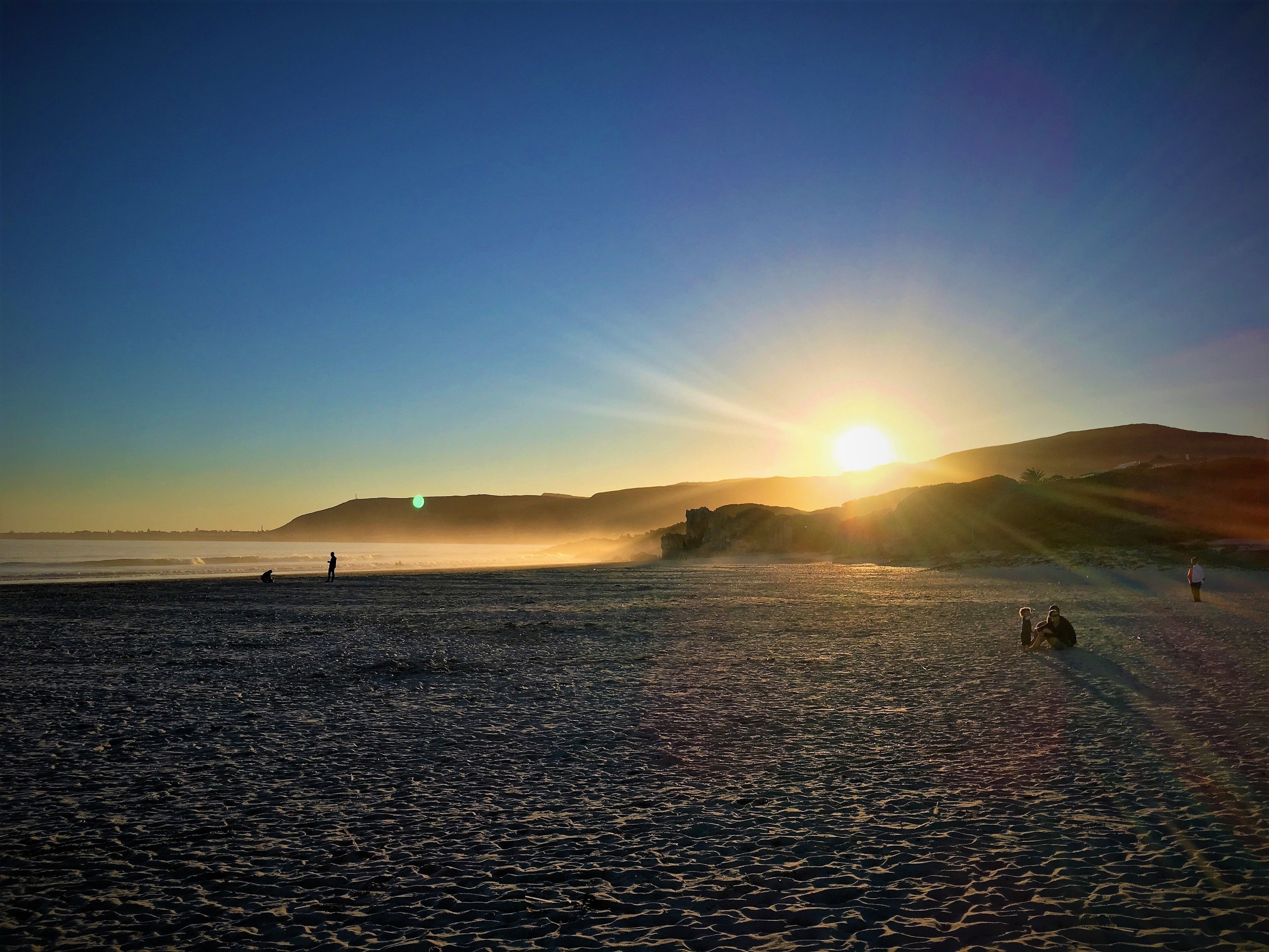A beach with a sunset, waves, and distant hills.