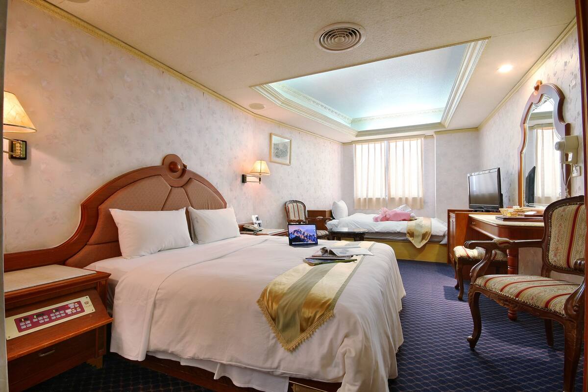 Una habitación de hotel con una cama grande, un escritorio, una silla, un televisor y una ventana con cortinas.